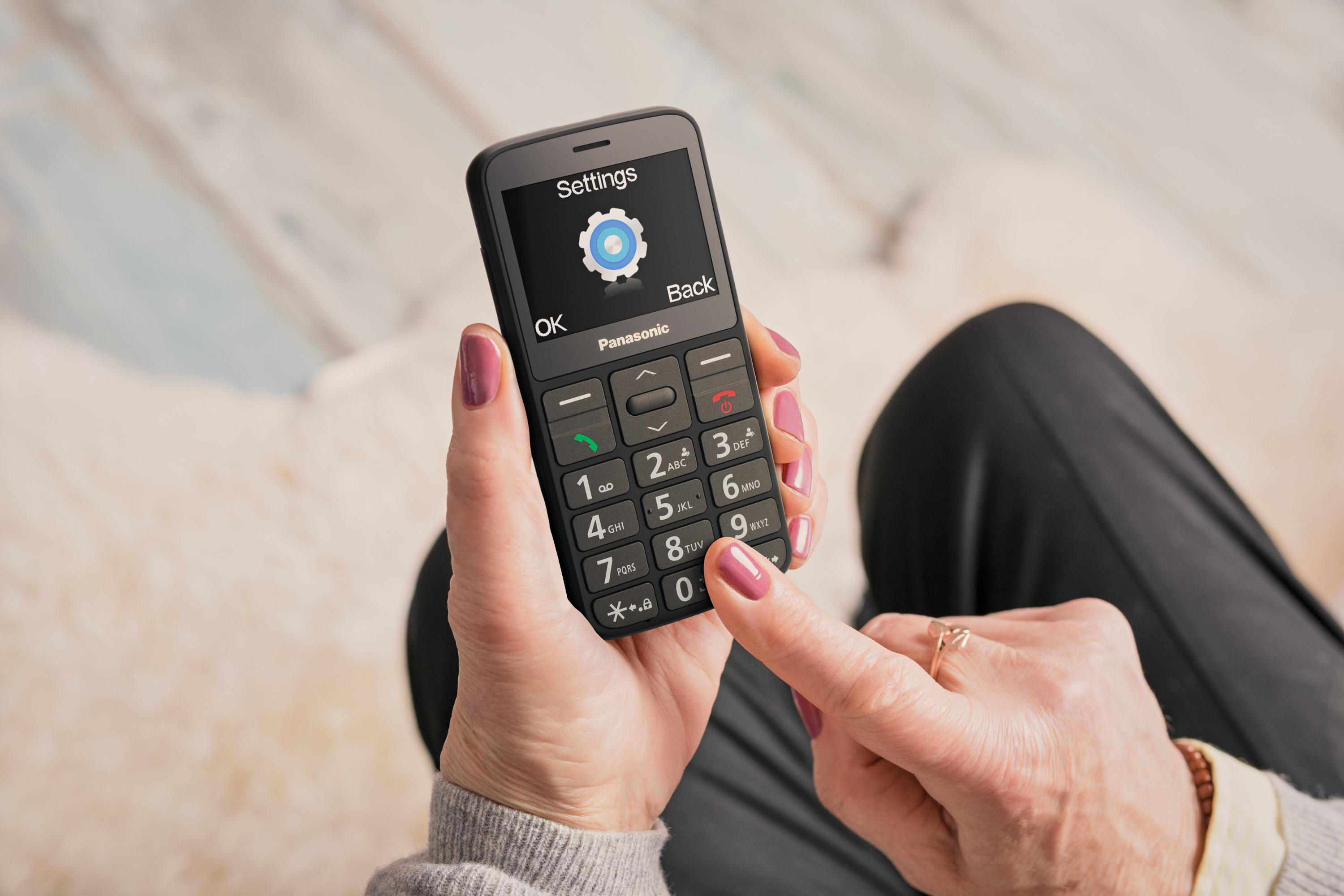 Eine Person hält ein schwarzes Panasonic-Telefon, das ein Einstellungsmenü anzeigt.