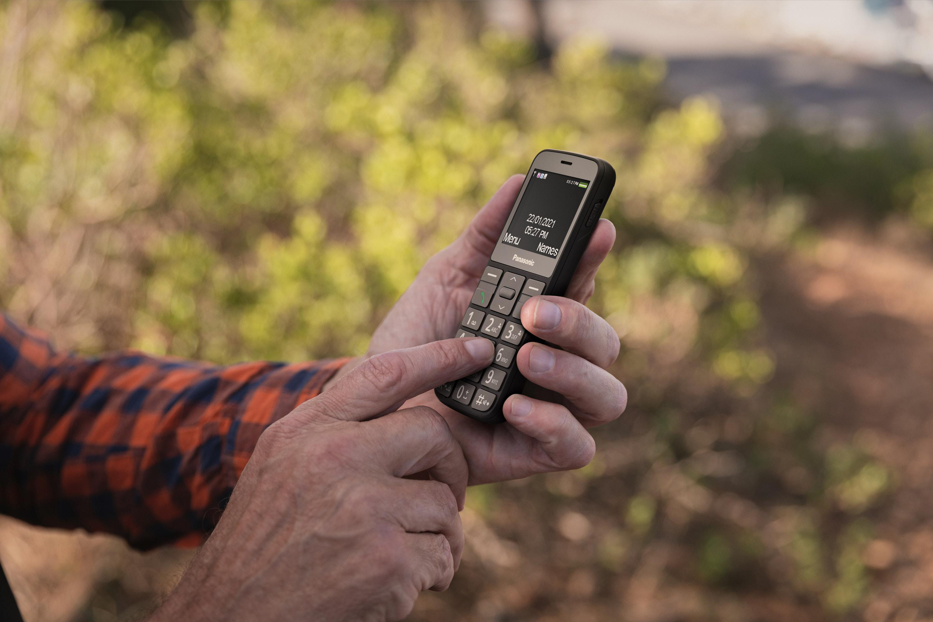 Person hält ein schwarzes Panasonic-Telefon mit Text auf dem Bildschirm.