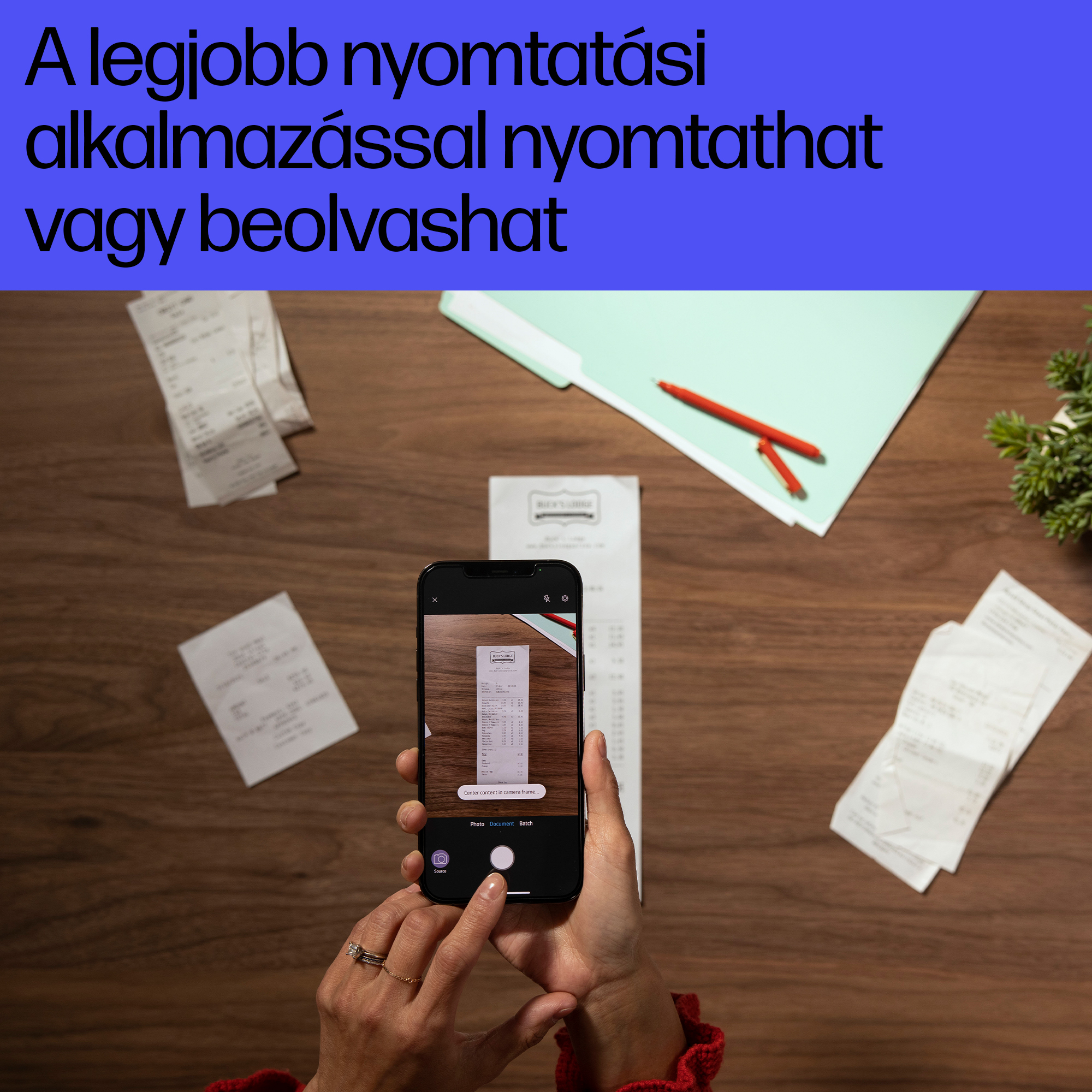 Egy telefon nyugtákat fotóz egy fa felületen, a közelben szétszórt nyugtákkal és tollal.