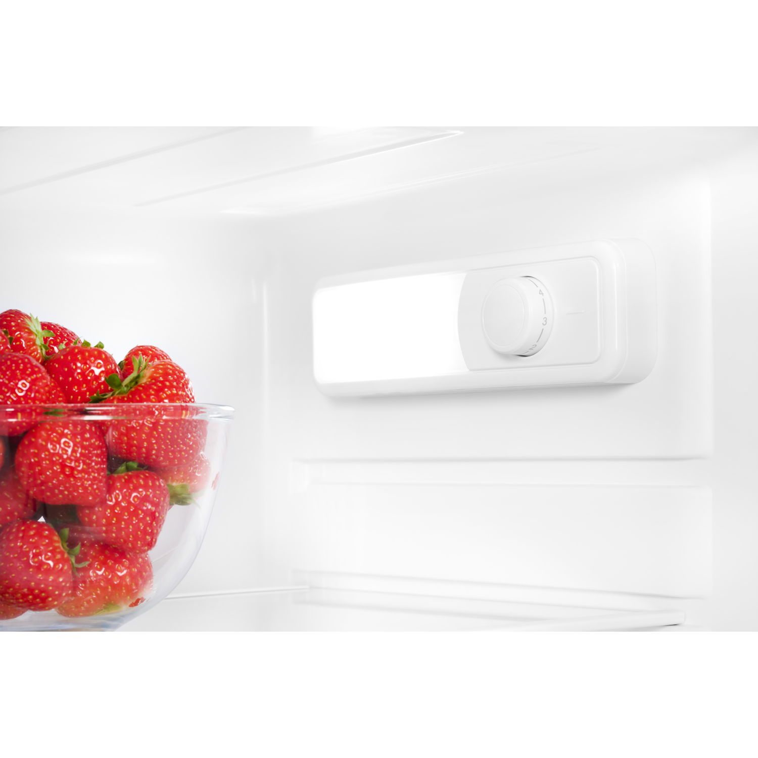 Inside a fridge with strawberries in a bowl, and a light and control panel on the wall.