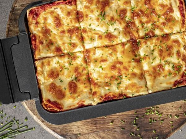 Draufsicht auf eine rechteckige Lasagne, in quadratische Portionen geschnitten.