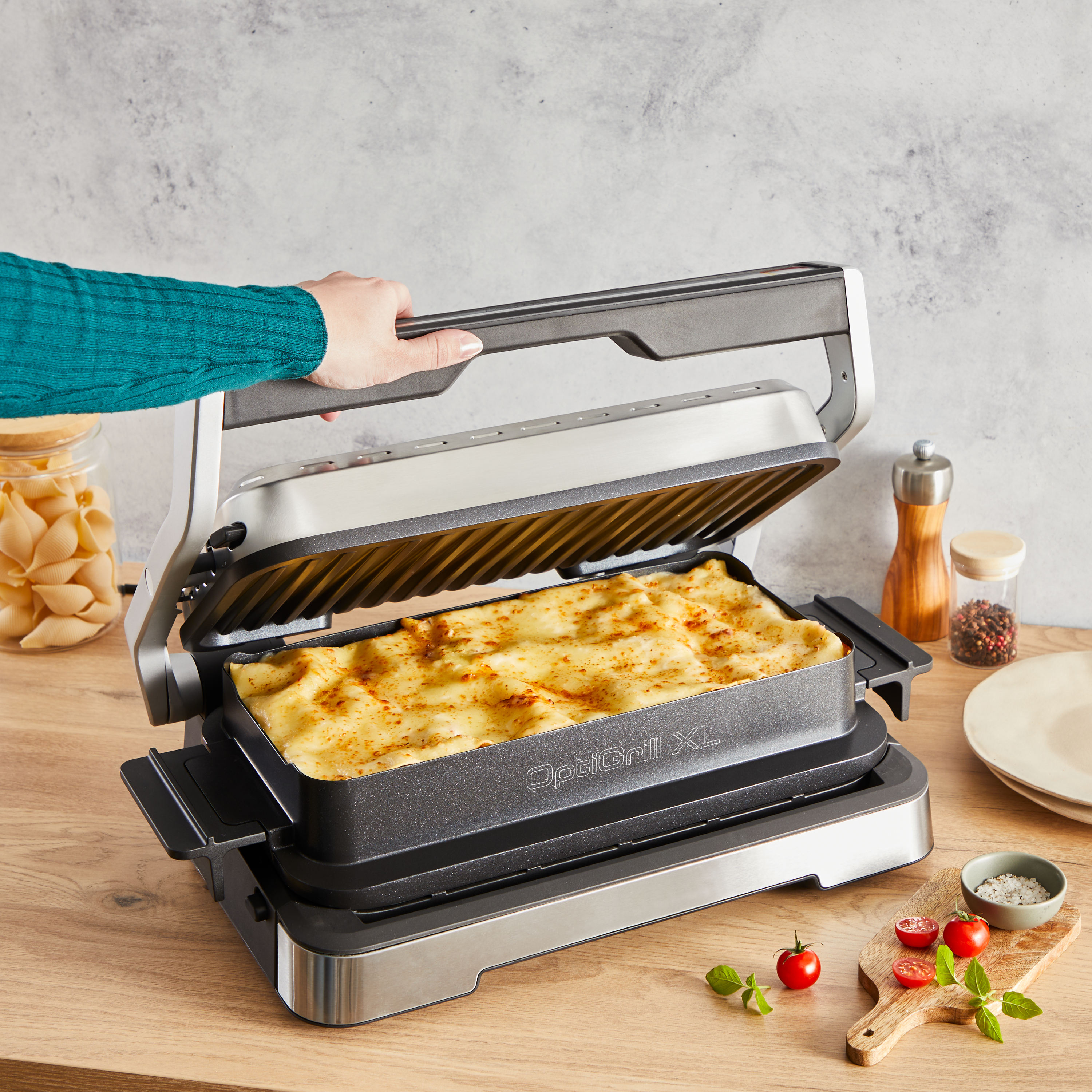 Eine Person hält einen Grilldeckel offen, um ein Gericht mit Lasagne zu zeigen.