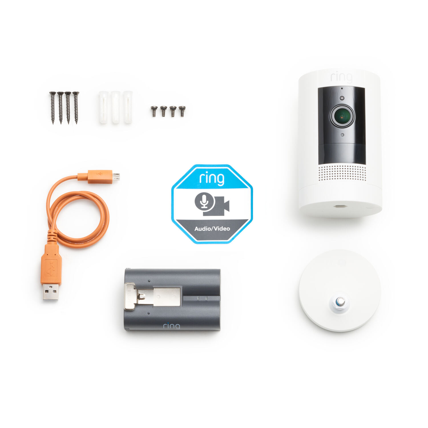 A security camera and its parts laid out on a white surface, with an orange charging cable.