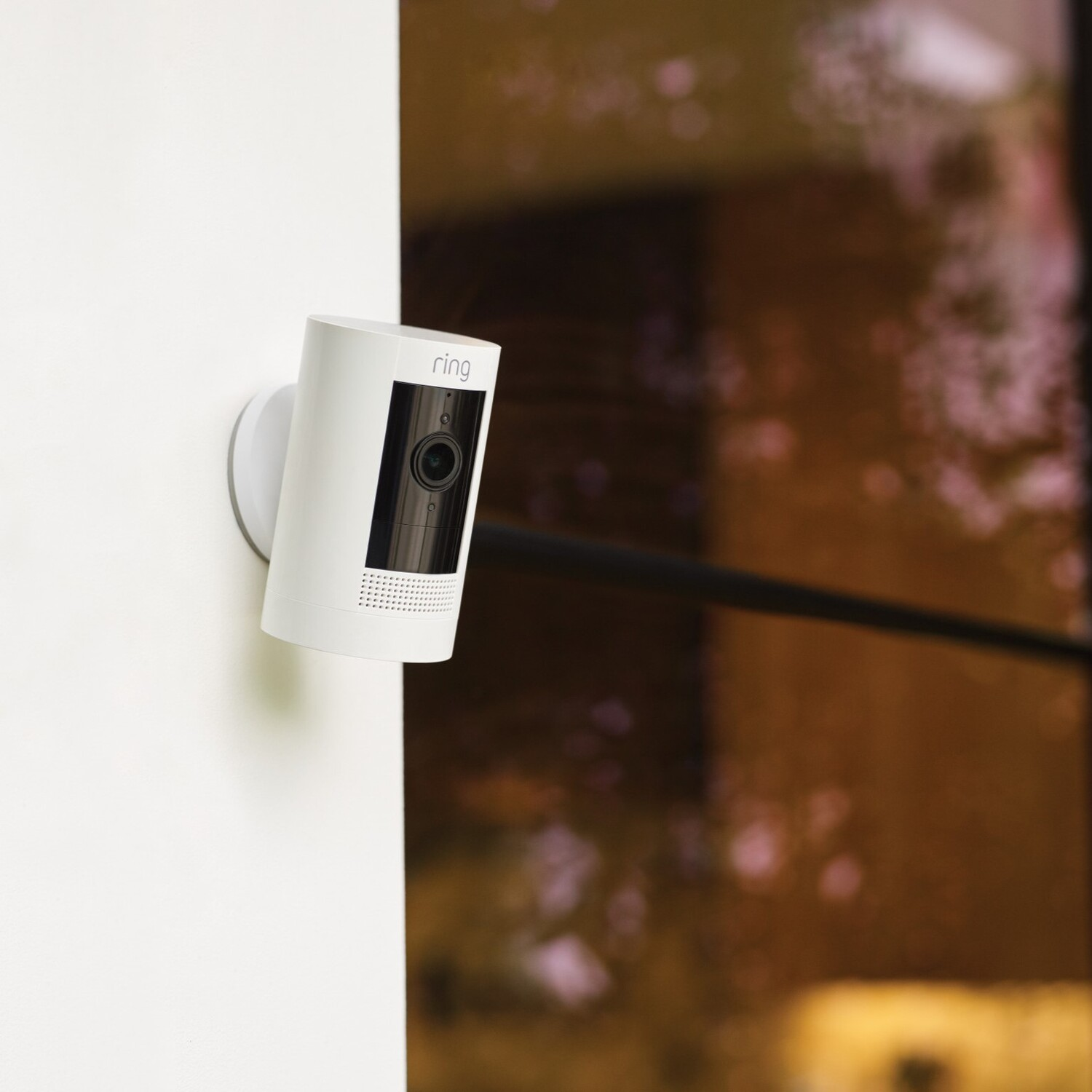 White Ring security camera mounted on a white wall. Night scene with soft lighting.