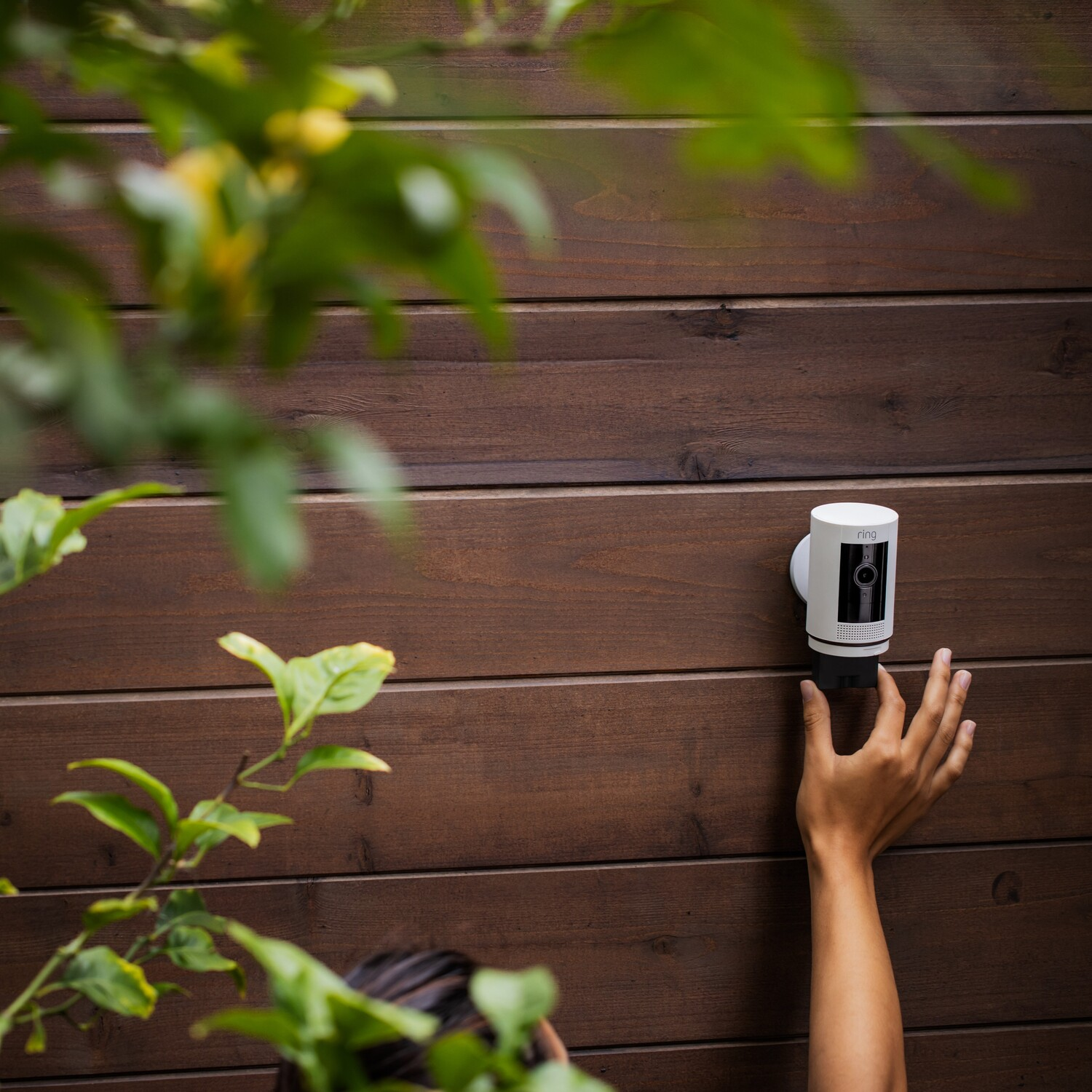 Hand installing a white security camera on a wooden wall.