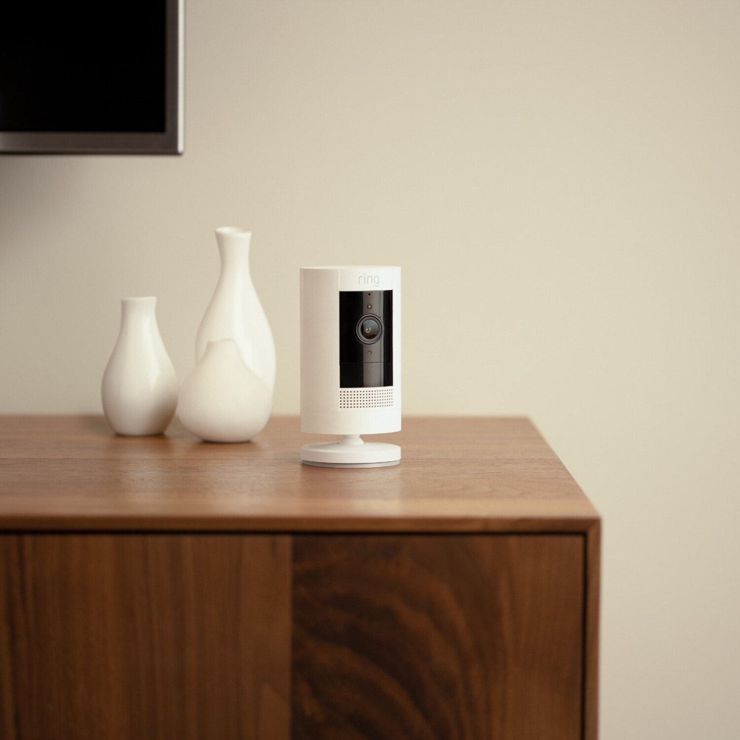A white Ring security camera on a wooden surface. Two white vases are to the left of the camera.