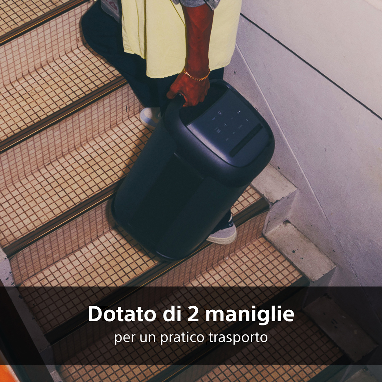 Una persona trasporta uno speaker portatile nero per le scale, con testo in italiano.
