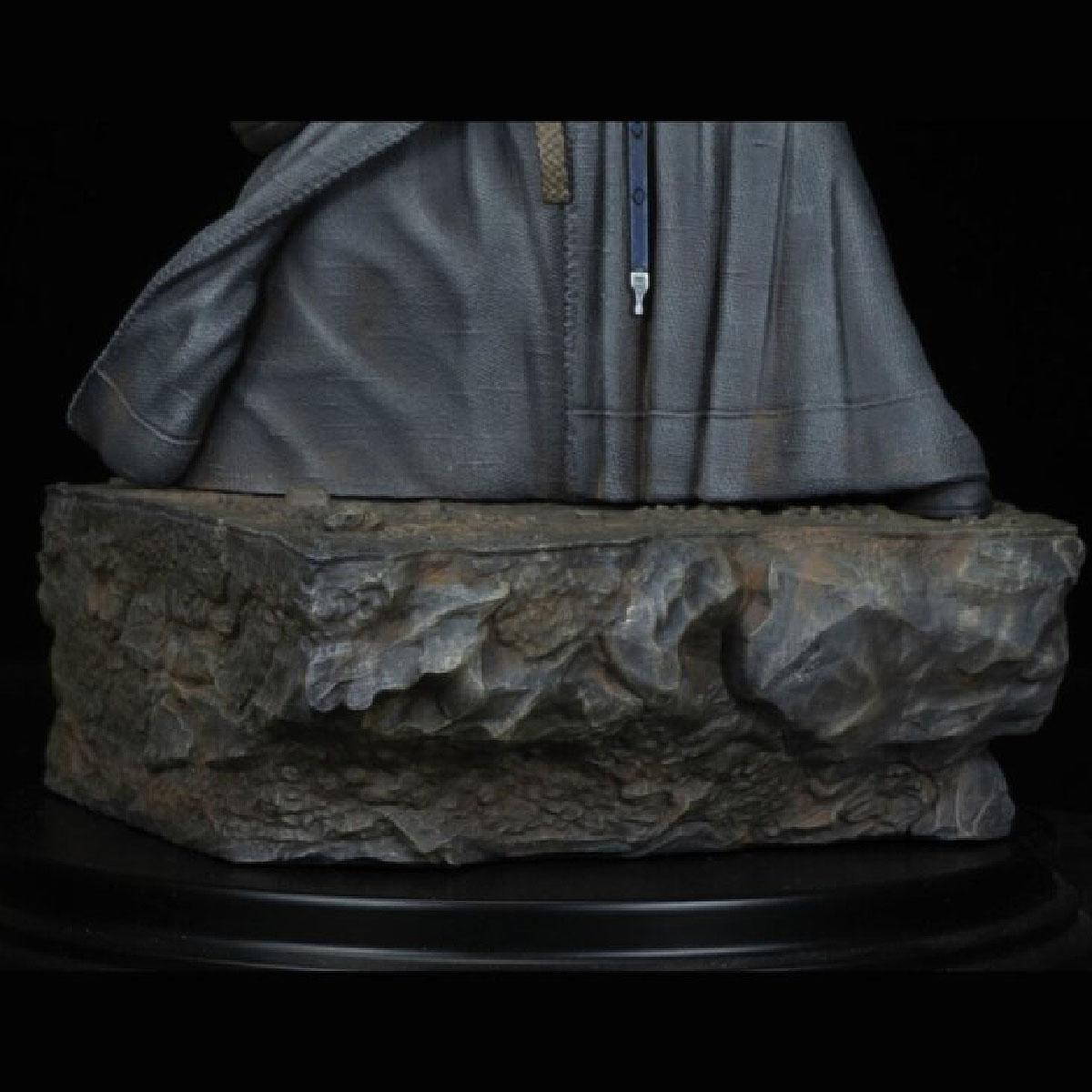 Statue einer Figur in einer Robe auf einem felsigen Sockel mit schwarzem Hintergrund.
