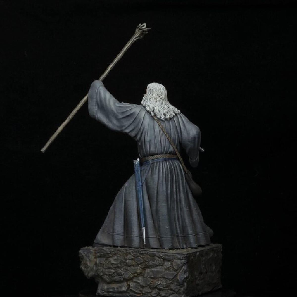 Gandalf-Statue von hinten, mit Stab, auf Steinsockel, schwarzer Hintergrund.