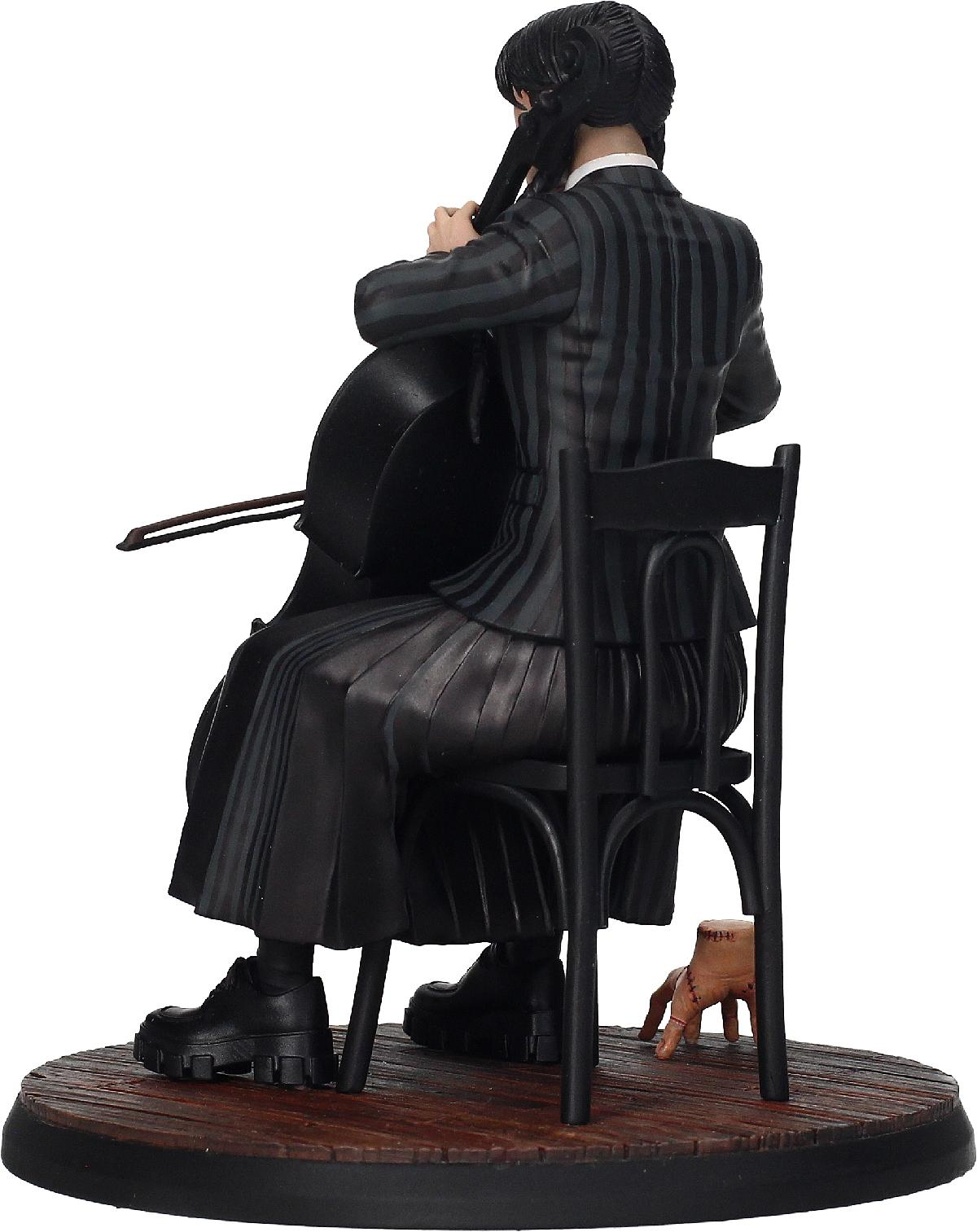 Eine Statue von Wednesday Addams, die Cello spielt, auf einem Stuhl sitzend. Eine Hand ist darunter sichtbar.