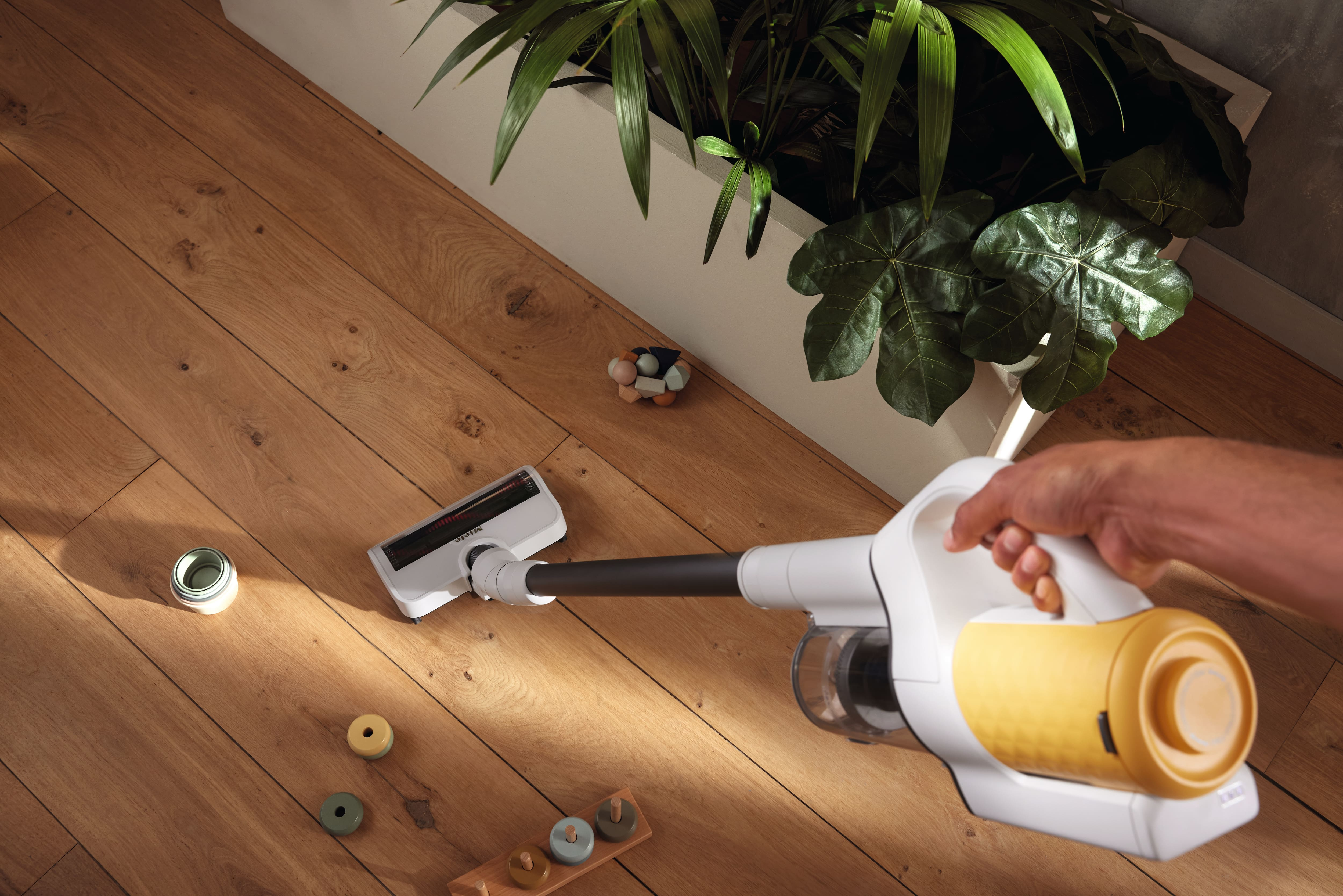 Eine Person saugt einen Holzboden mit einem kabellosen Staubsauger.