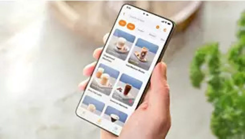 Ręka trzymająca telefon z wyświetlonym menu napojów kawowych.
