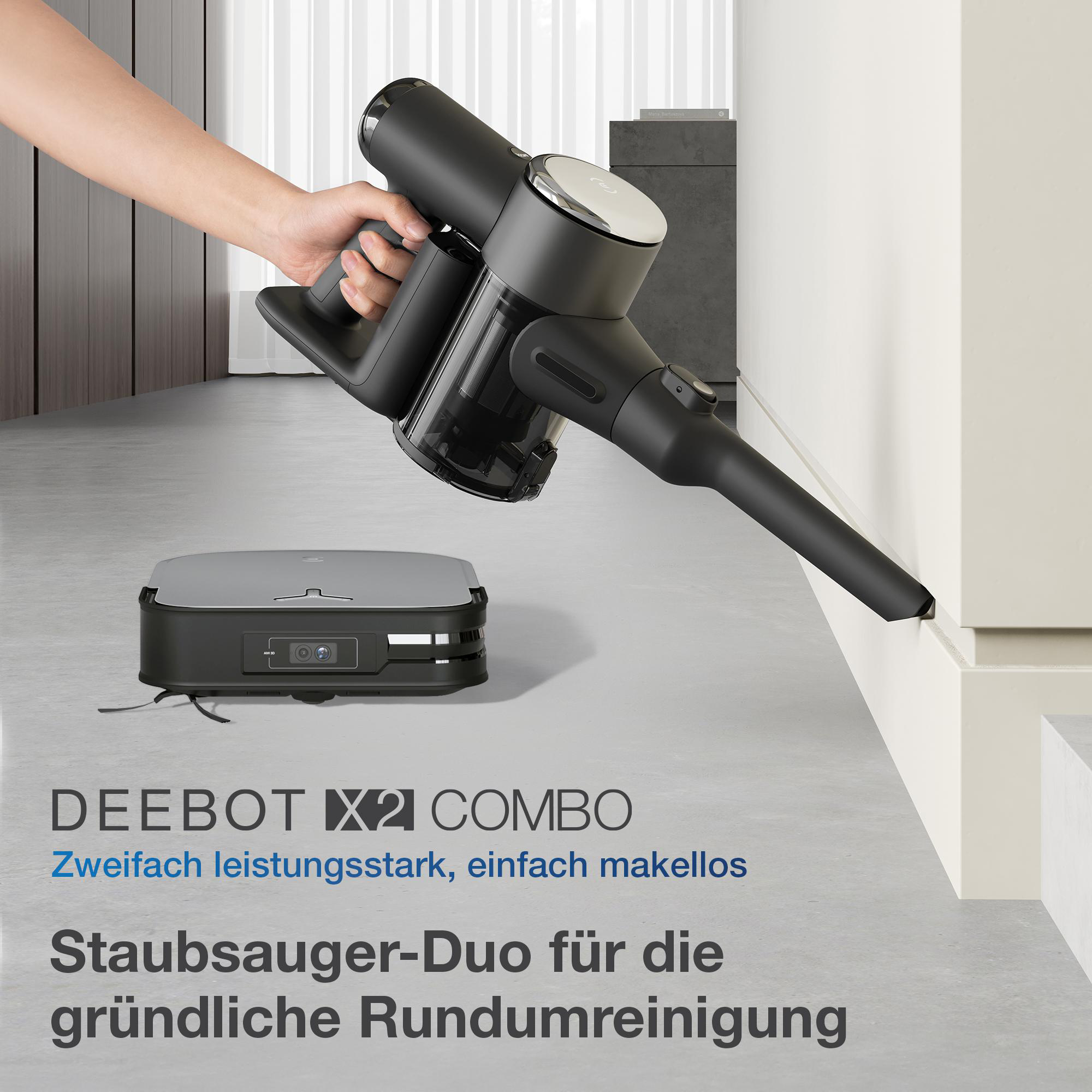 Eine Person benutzt einen schwarzen Staubsauger mit einem grauen Roboterstaubsauger. Grauer Boden und weiße Wand im Hintergrund.