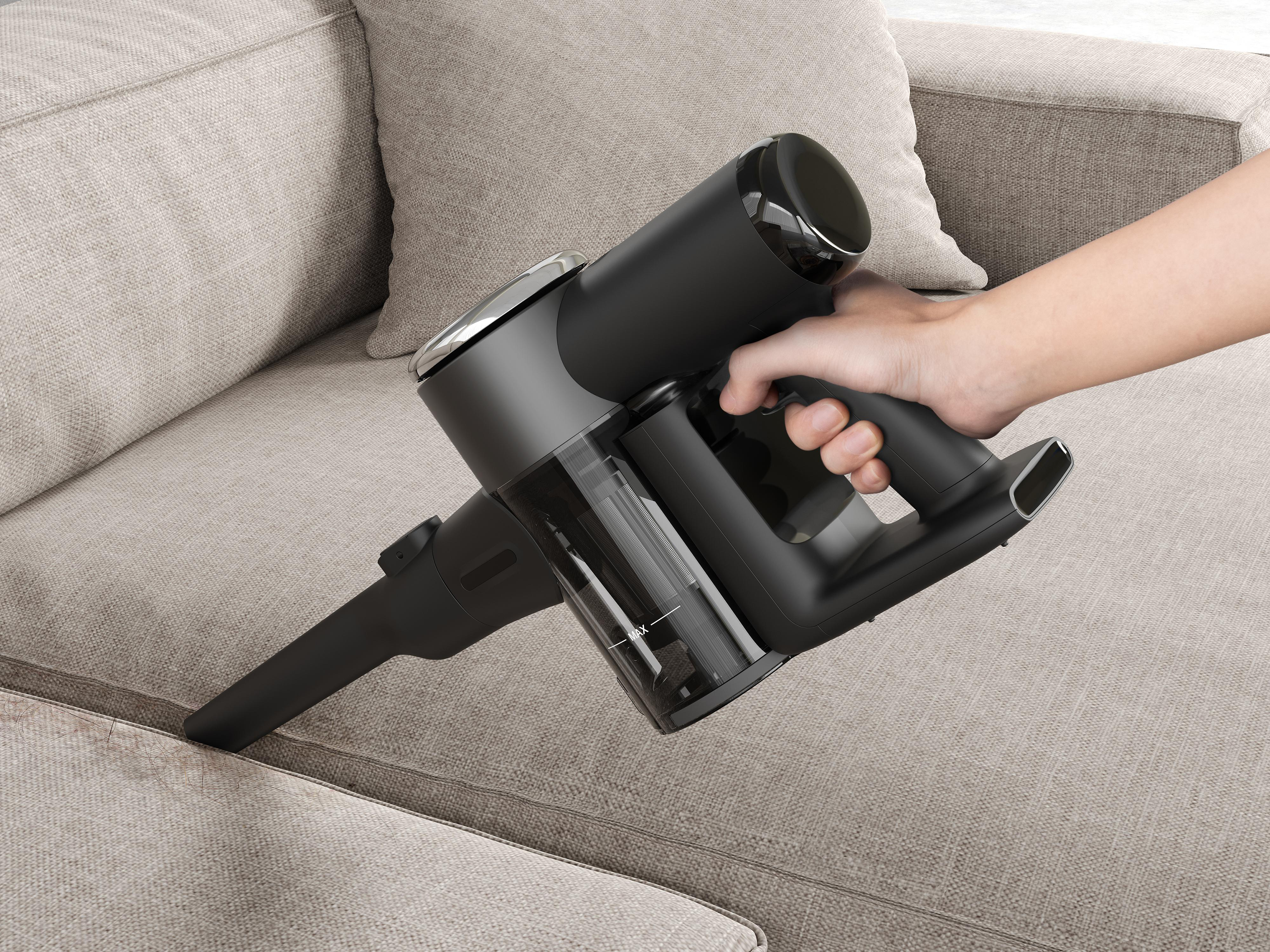 Eine Hand benutzt einen schwarzen Staubsauger auf einem beigen Sofa.