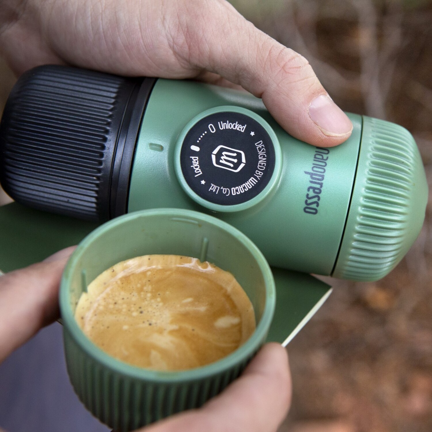 Handen houden een groene Nanopresso met koffie vast. Een groen boek ligt op het oppervlak.