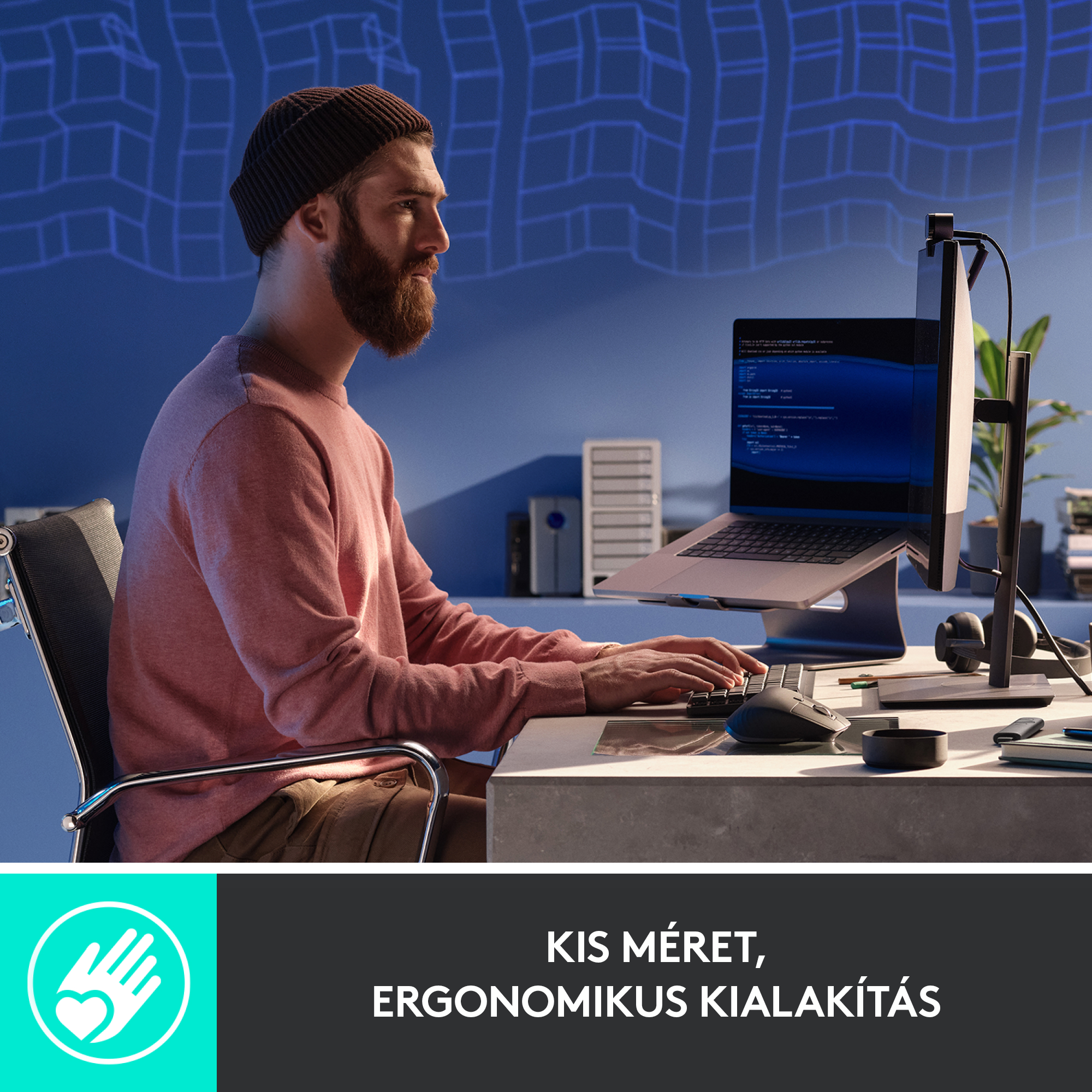 Szakállas, kalapos férfi laptopon dolgozik külső monitorral, íróasztalon.