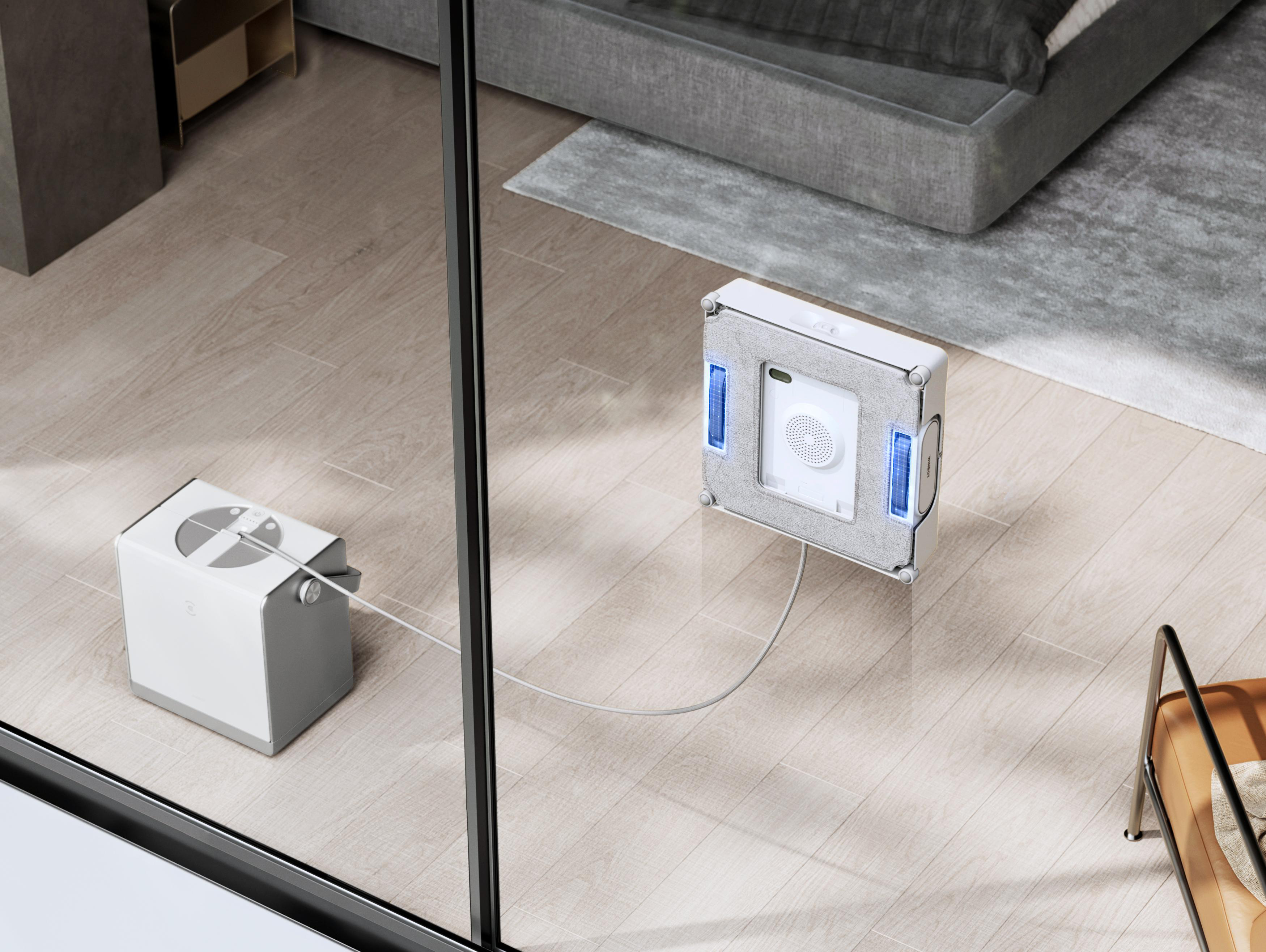 Roboter-Fensterreiniger an einem Fenster. Daneben eine Ladestation. Der Boden ist aus Holz.
