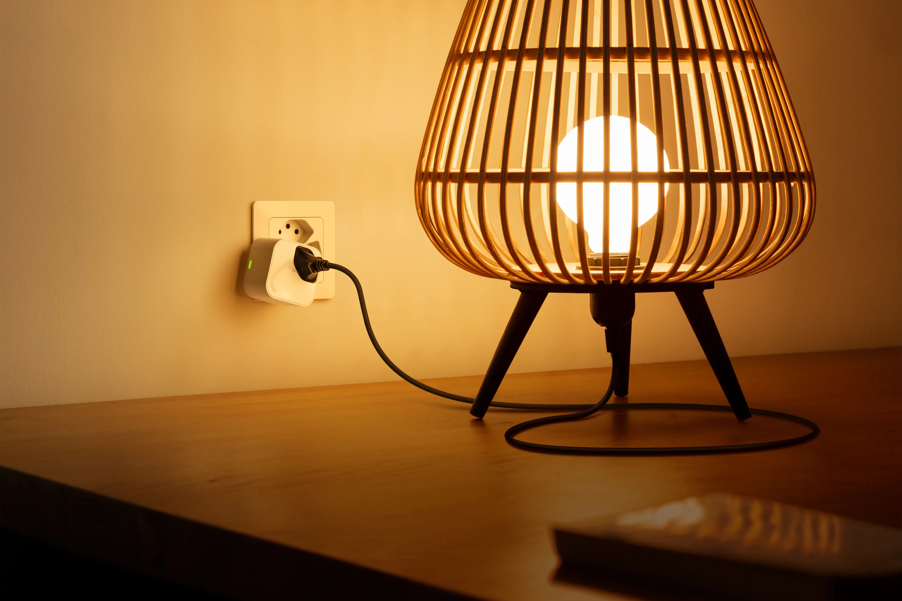 Eine Lampe mit gewebtem Lampenschirm ist beleuchtet, eingesteckt und steht auf einem Holztisch.