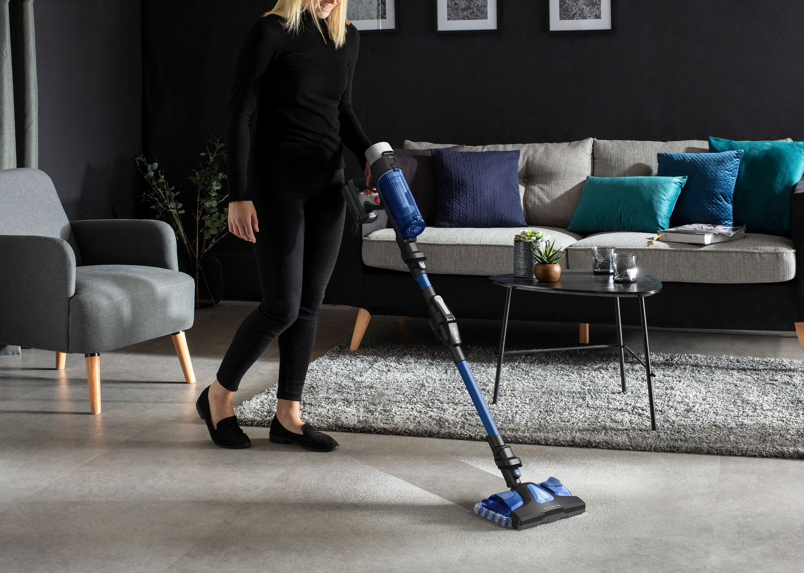 Mujer aspirando una habitación con una aspiradora azul y negra.