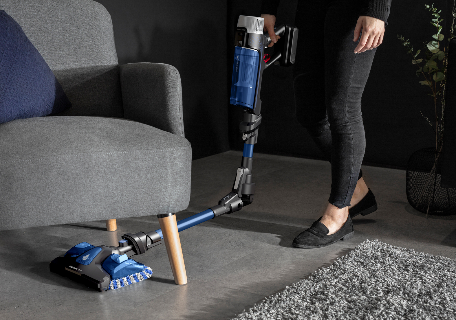 Persona aspirando debajo de los muebles con una aspiradora inalámbrica azul y negra.
