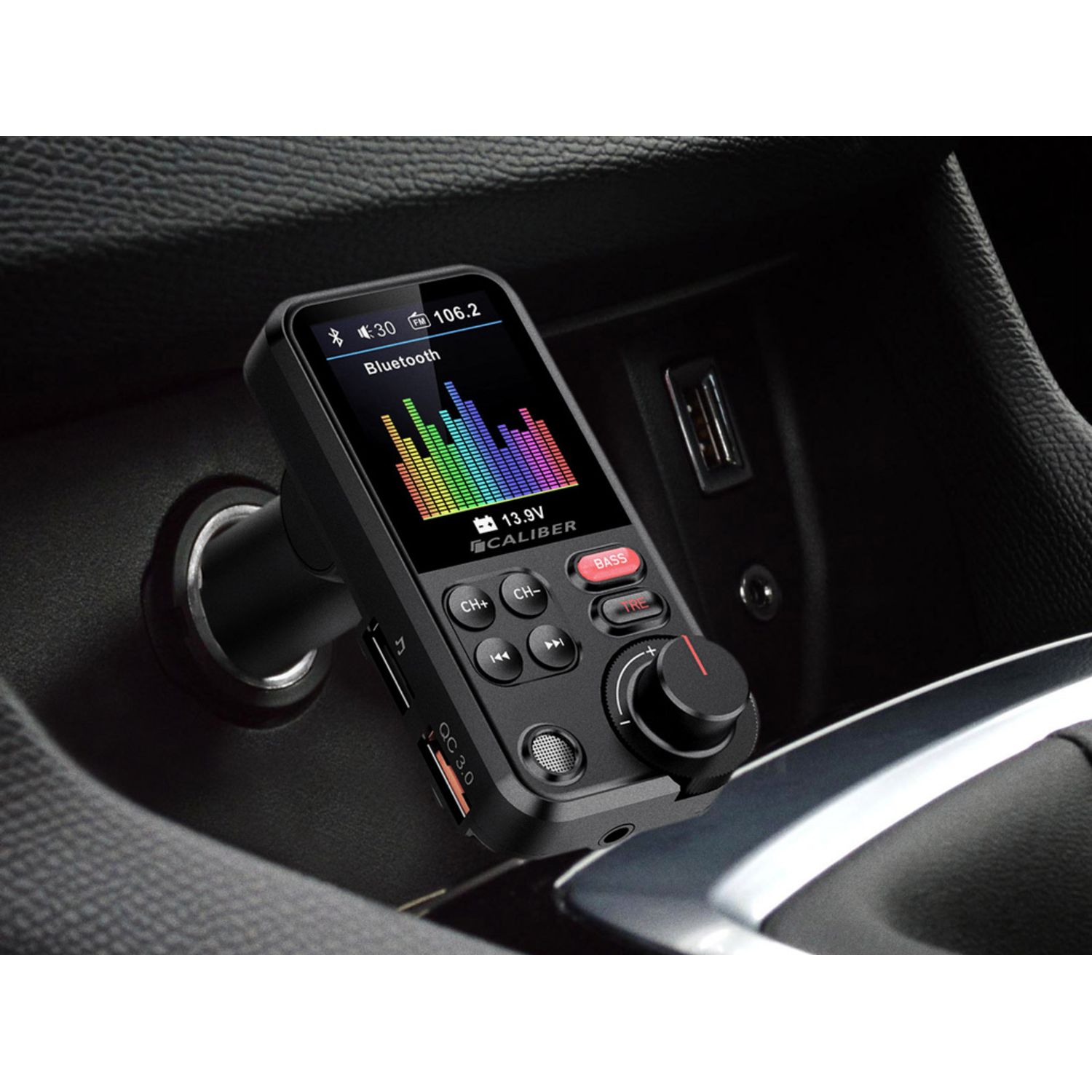 Black car FM transmitter with screen, buttons, and knob. Placed in a car's console.