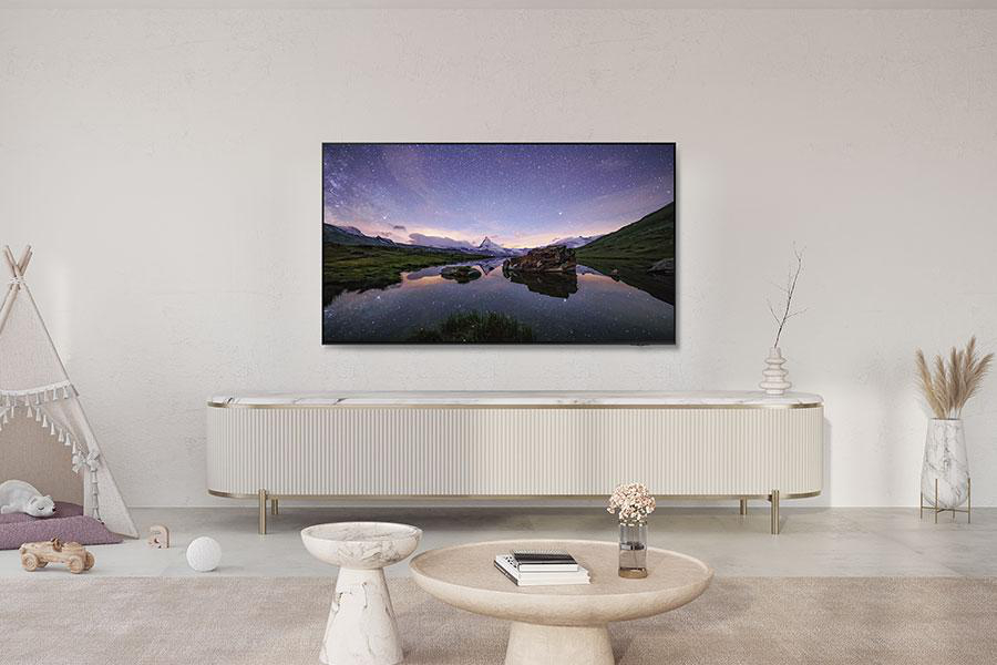 Ein Fernseher an der Wand, der eine Landschaft reflektiert. Eine weiße Kommode und ein runder Tisch davor.