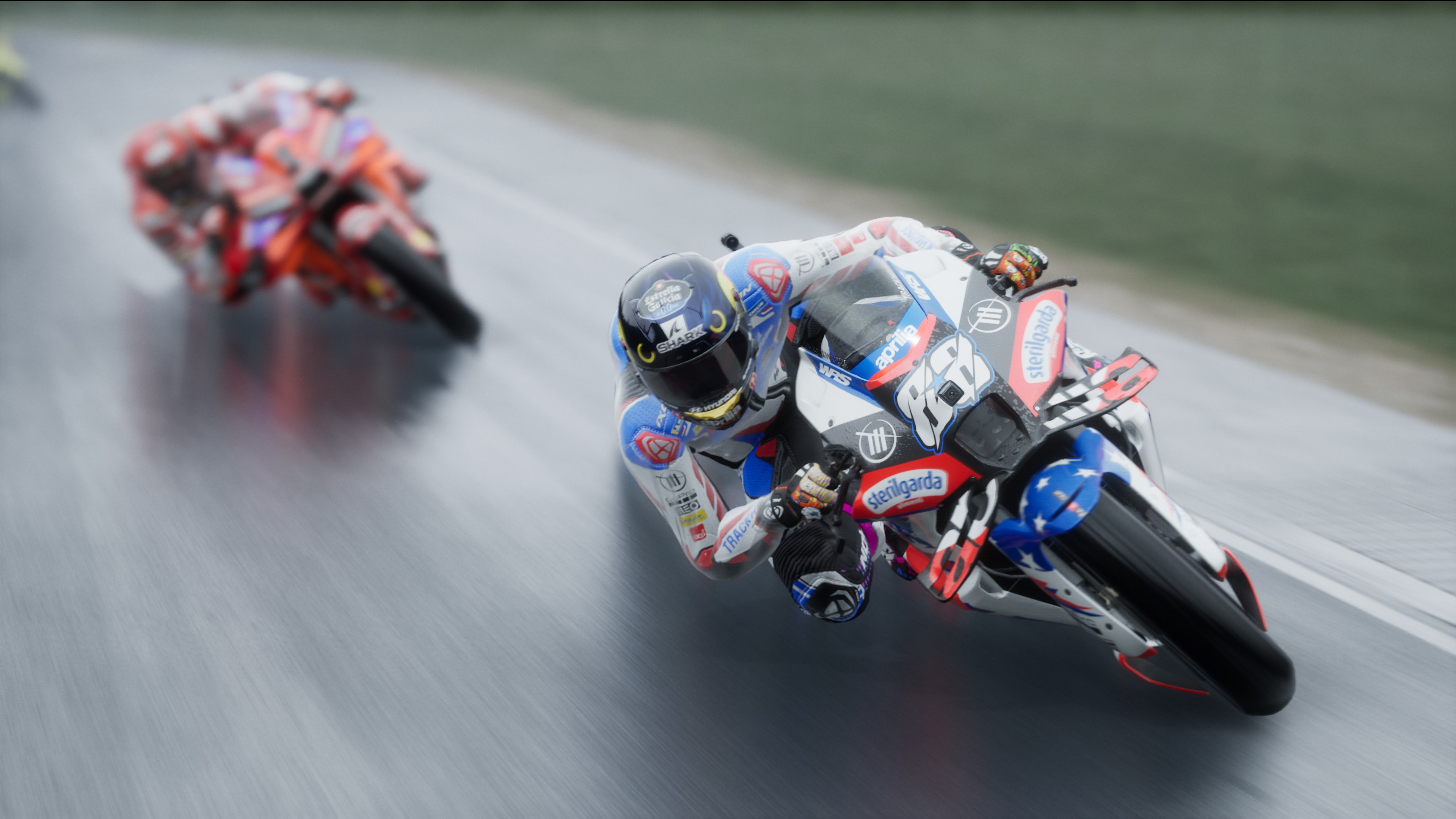 Des coureurs de motos sur une piste, un en gros plan au premier plan. Les motos ont des logos de sponsors et sont inclinées.