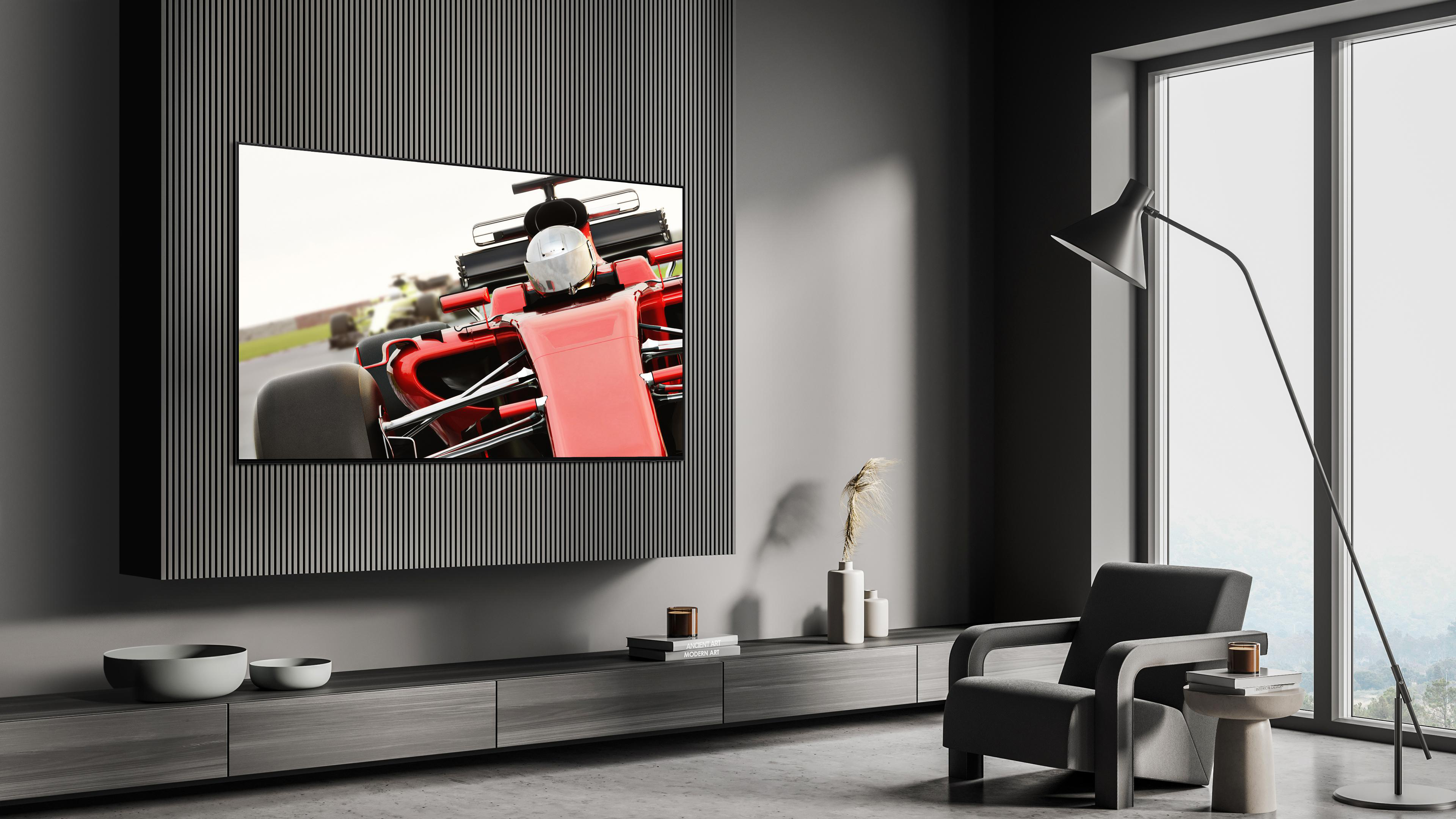 Wohnzimmer mit TV, der ein Rennauto zeigt. Ein schwarzer Sessel und ein Fenster sind sichtbar.