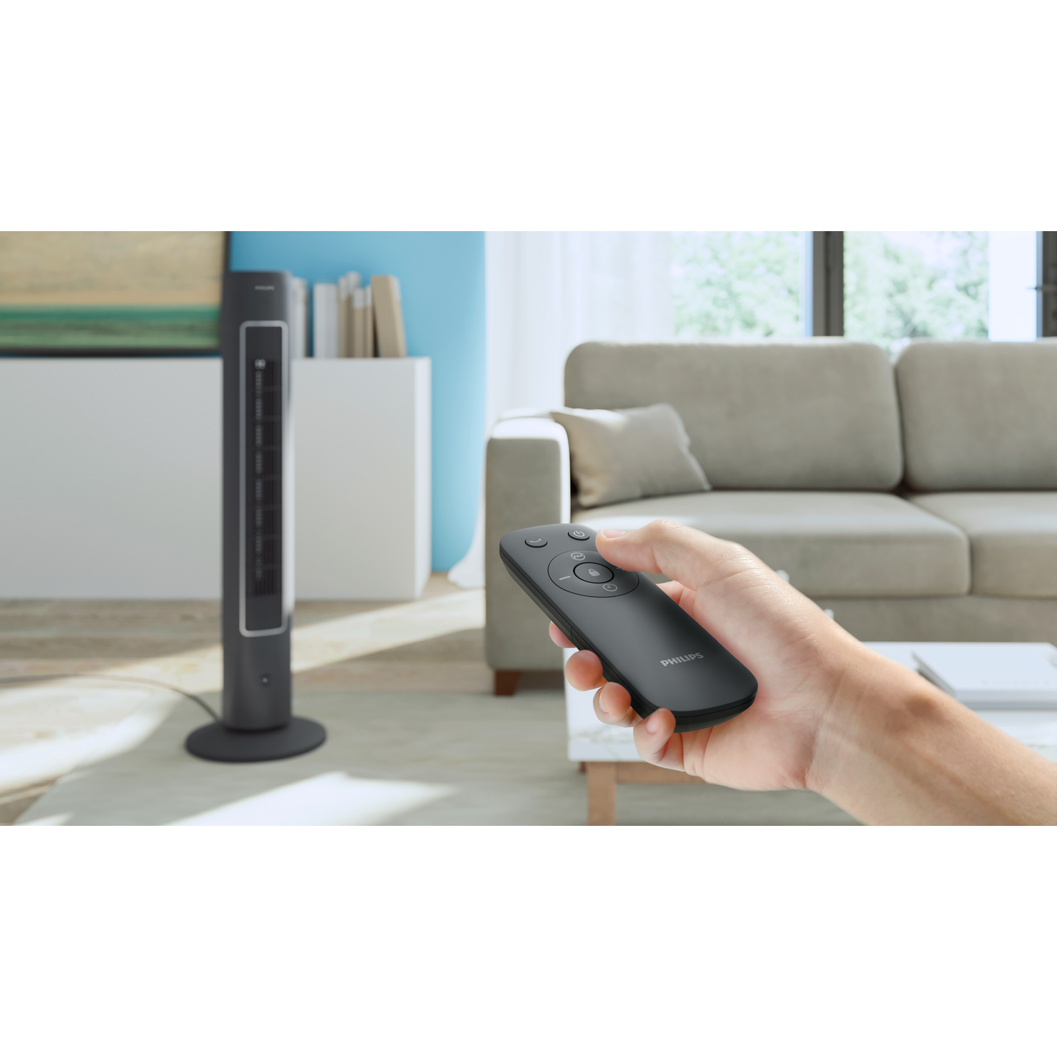 Person's hand holding a remote control. A black fan is in the background.