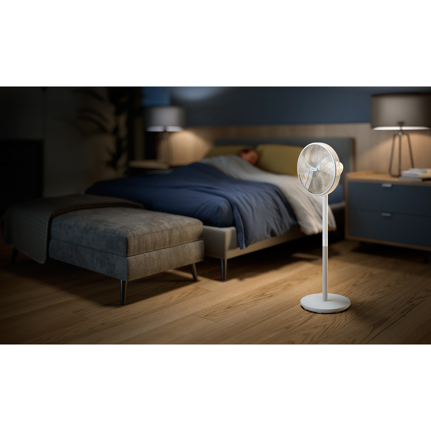 Bedroom scene with a stand fan and a bed. A person is sleeping on the bed.