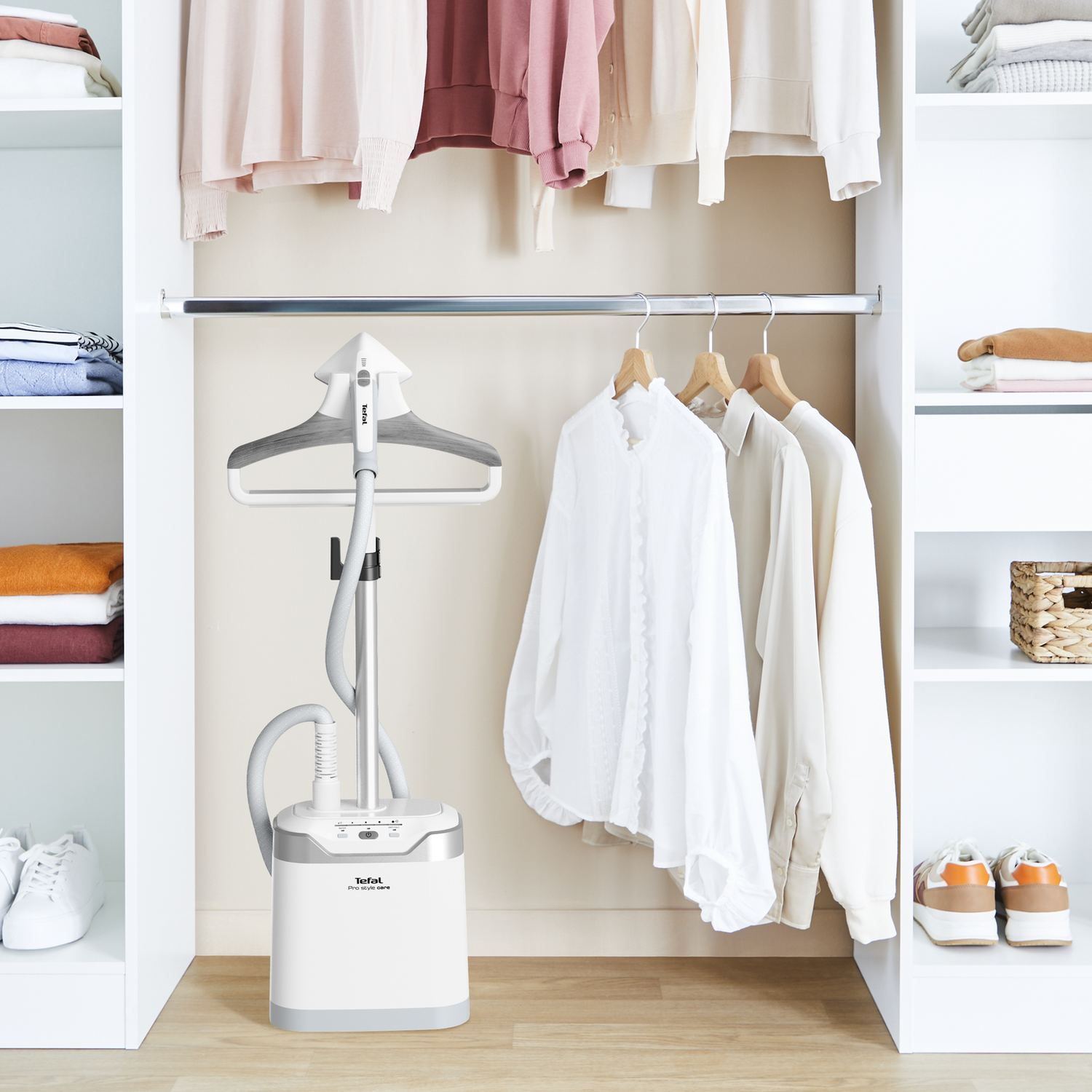 A clothing steamer next to a rack of clothes inside a closet. White and neutral colors.