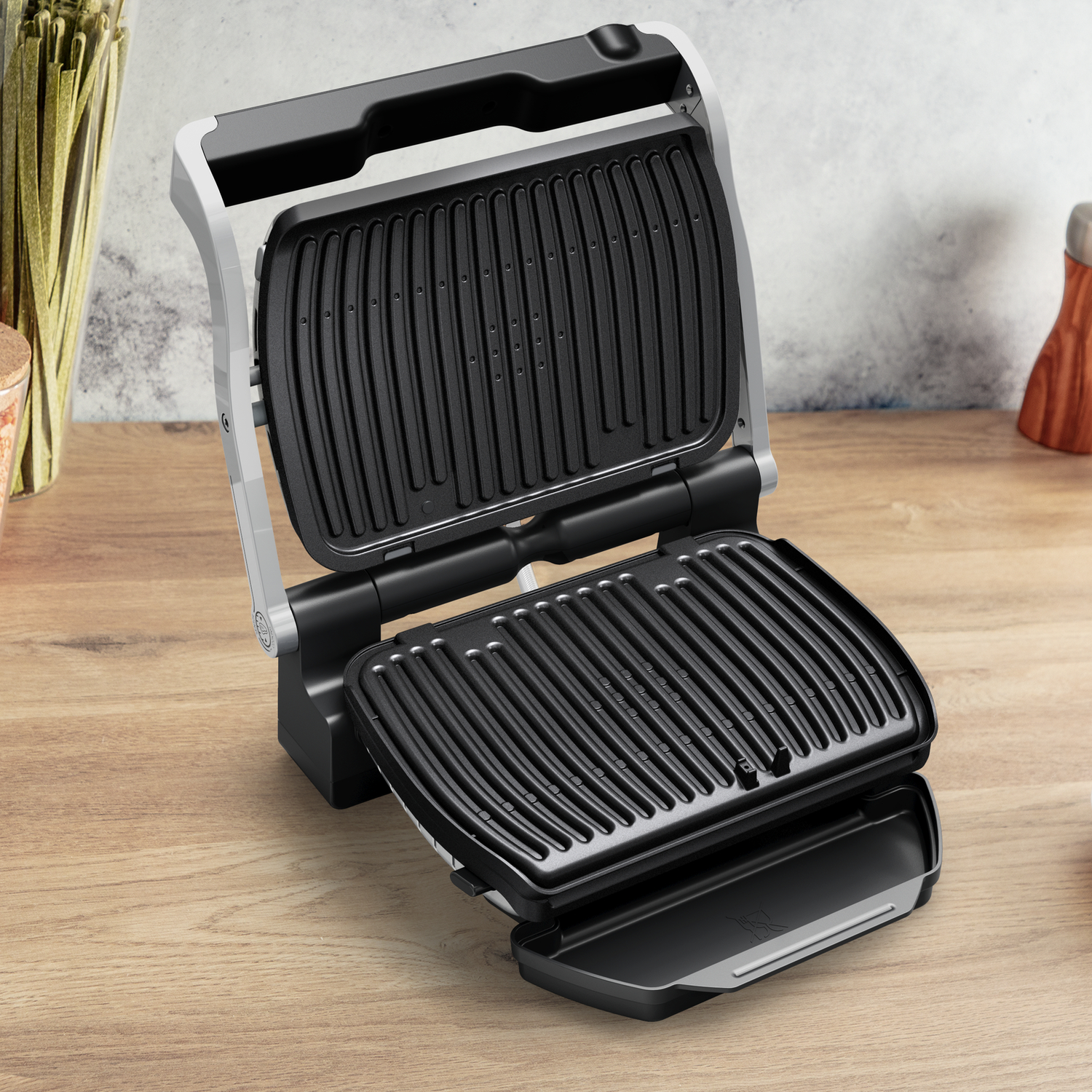 Open grill op houten tafel. Zwarte grillplaten, grijze frame. Keukengerei op de achtergrond.