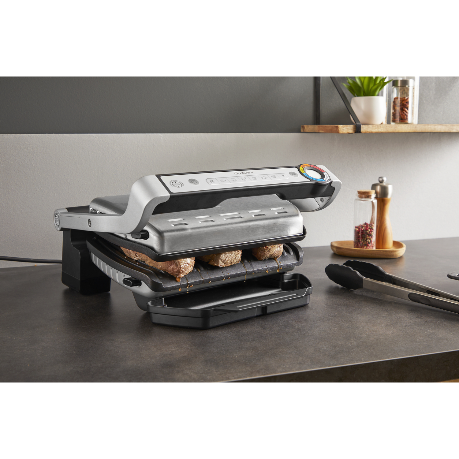 Een grill met steaks die erop bakken. Tangen en andere items liggen eromheen.