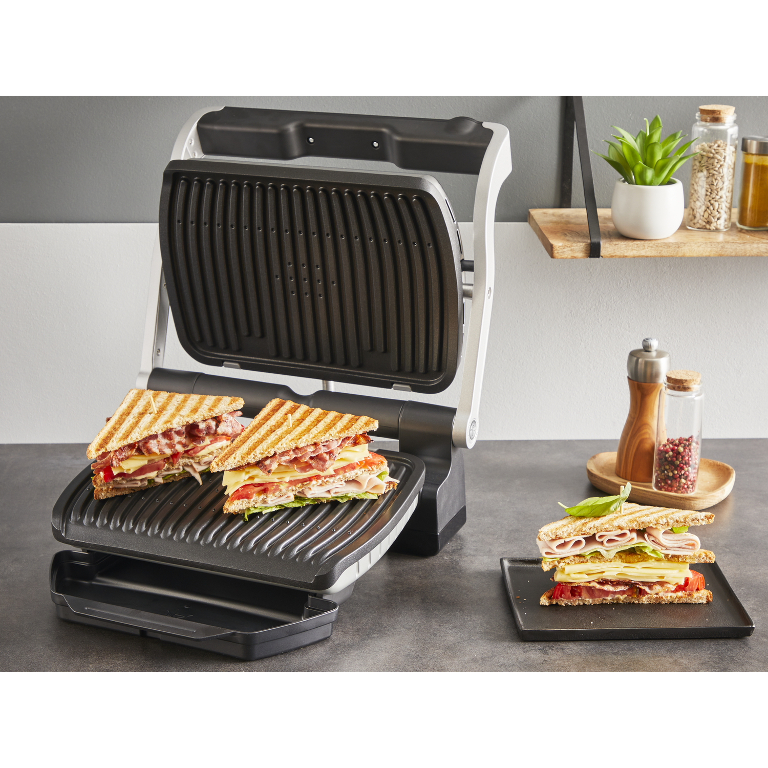 Een panini grill met twee sandwiches op de grill en één op een bord.