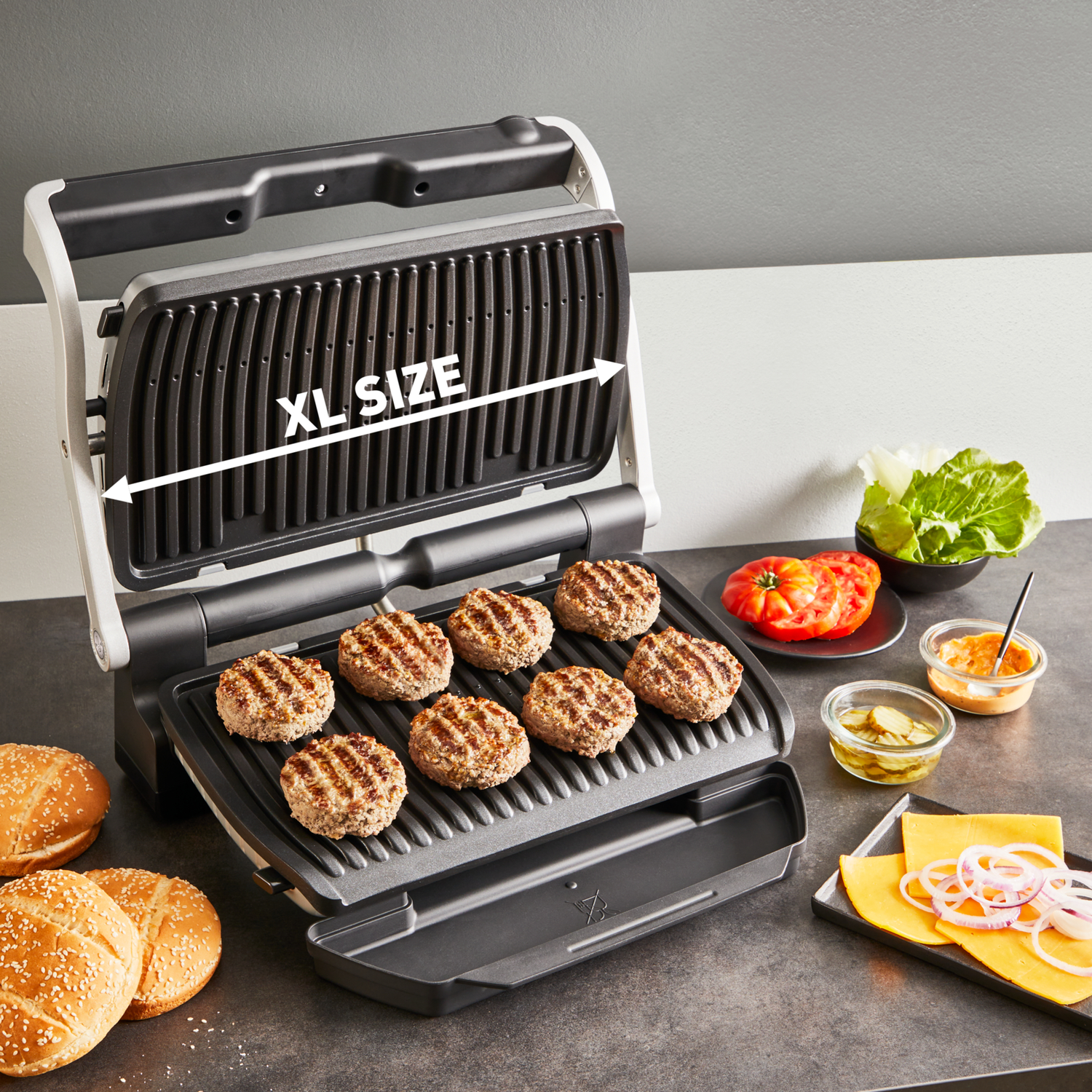 XL sized grill with burgers. Buns, toppings, and sauces are near the grill.
