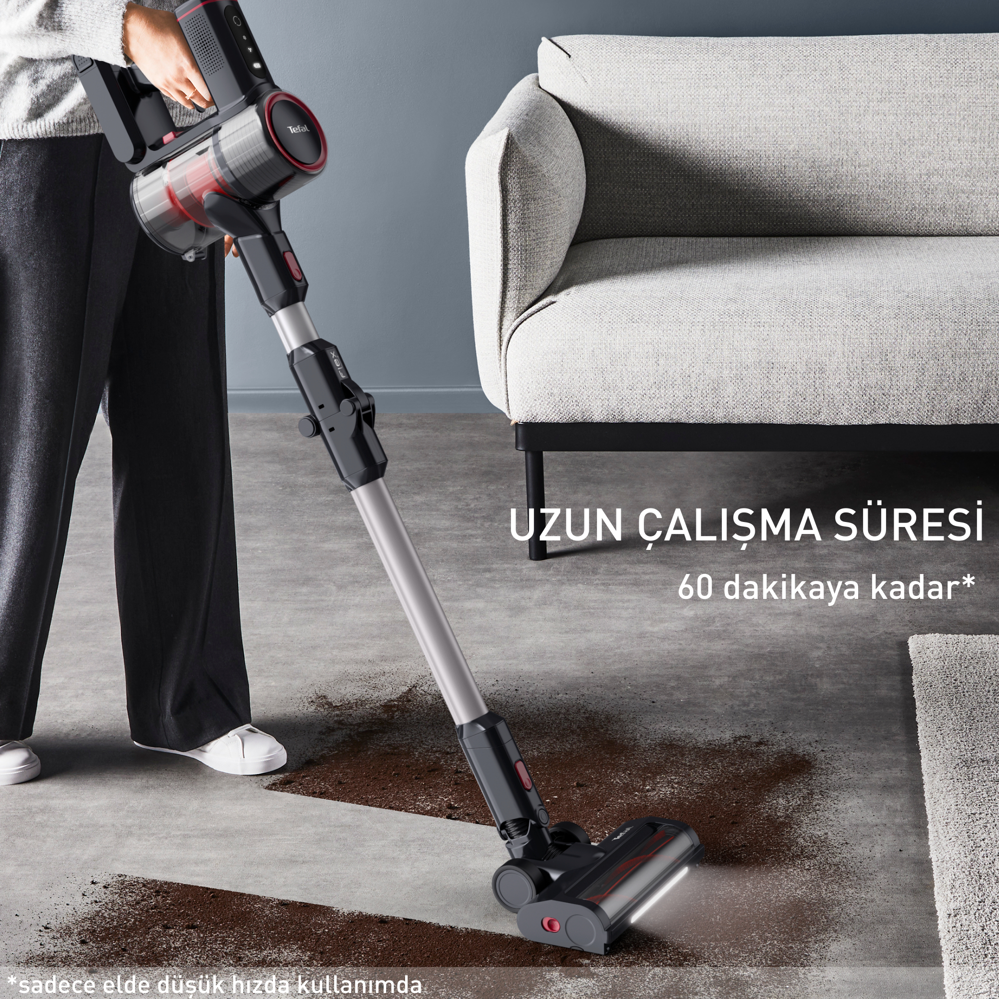 Halı kaplı bir zeminde siyah ve kırmızı kablosuz bir elektrikli süpürge kullanan bir kişi.