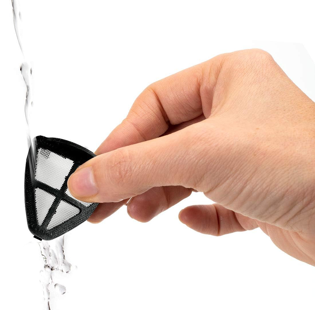 Ręka trzymająca czarny filtr do kawy pod bieżącą wodą na białym tle.