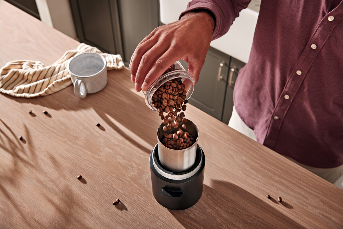Person gießt Kaffeebohnen in eine Kaffeemühle.