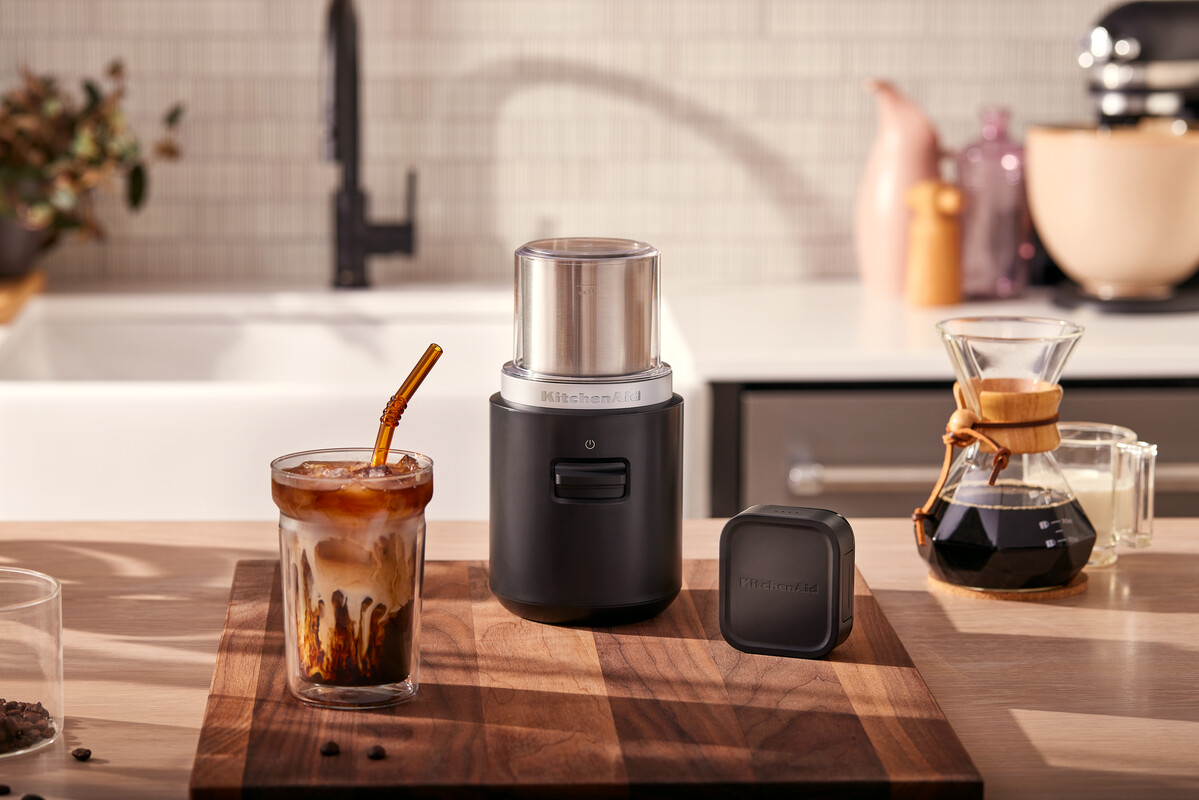 Kaffeemühle, Kaffee und Glas mit Eiskaffee. Holzbrett, Küchenhintergrund.
