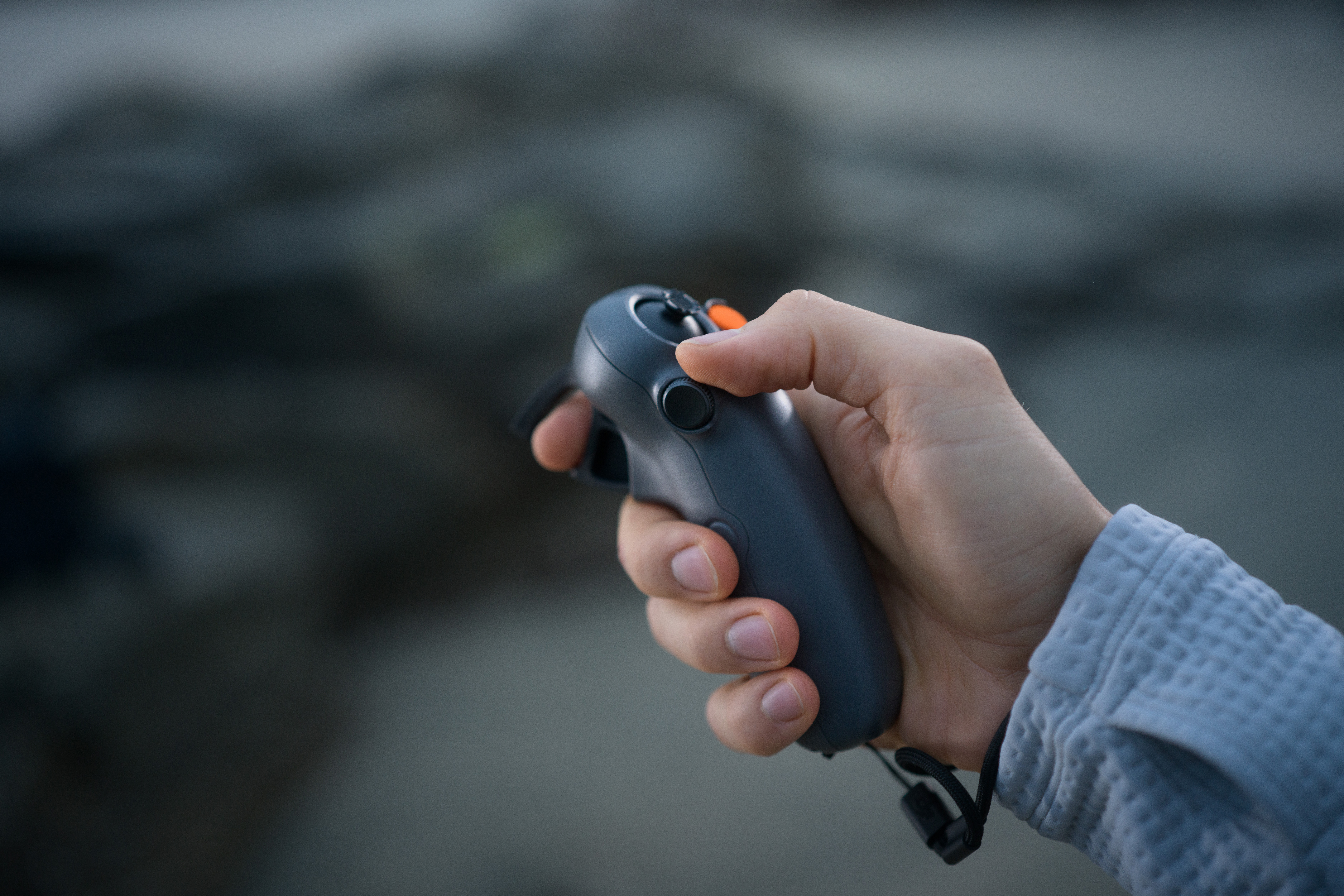 Personne tenant une manette de jeu gris foncé. La manette a des boutons et un joystick. Fond flou.