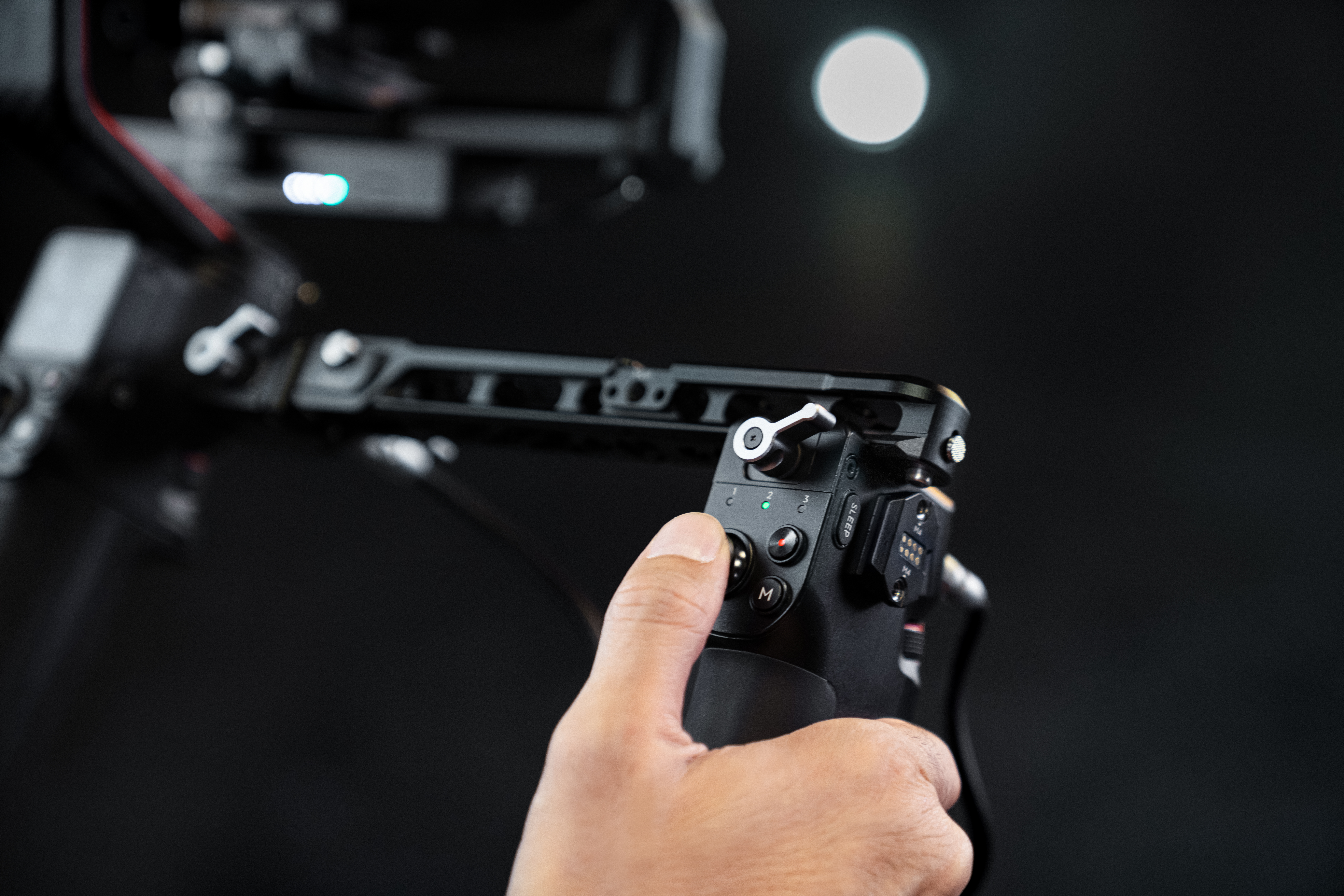 Main tenant une manette de caméra noire. Boutons et molettes visibles sur l'appareil.