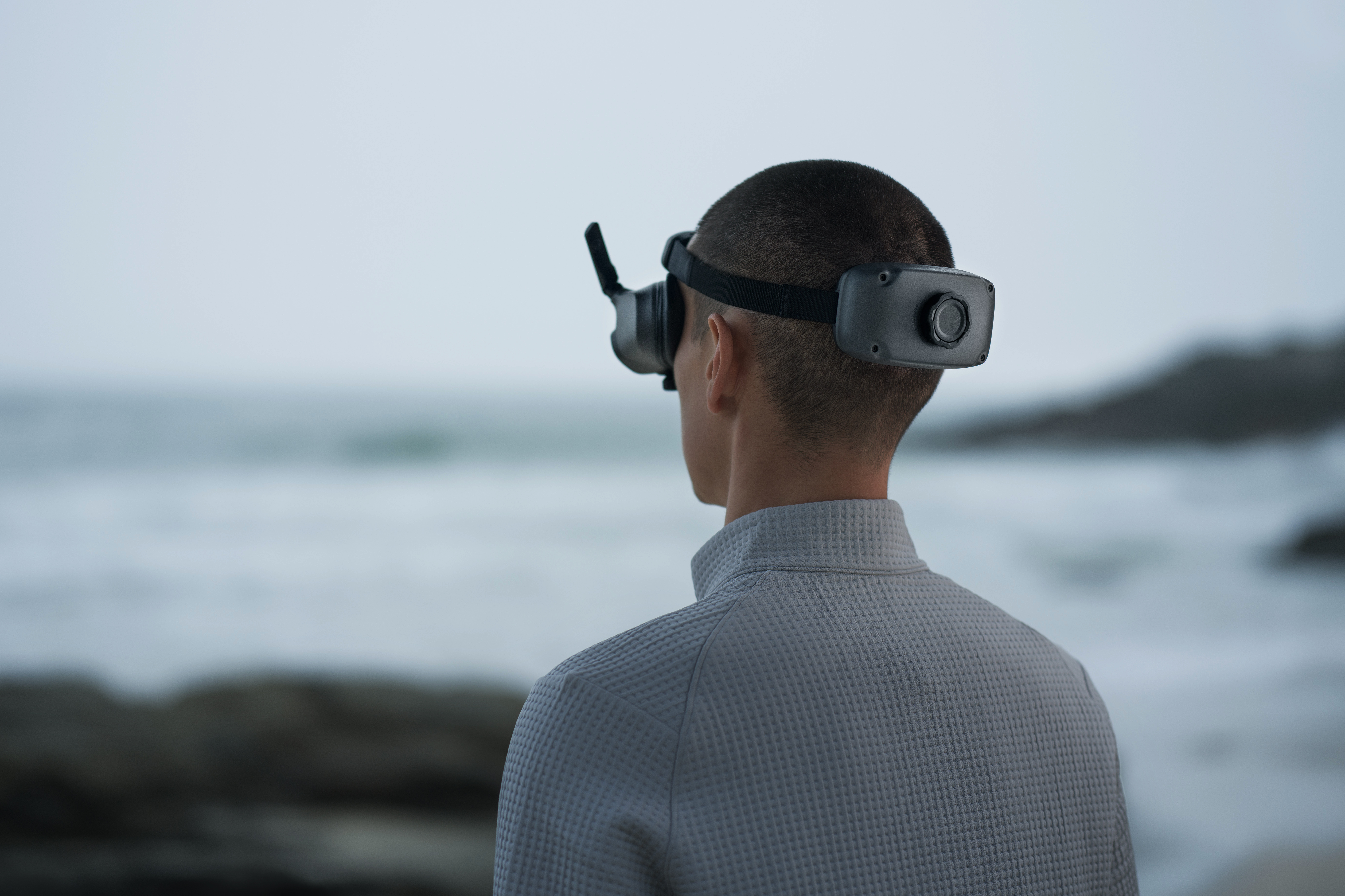 Une personne portant des lunettes VR regarde une vue floue de l'océan. Elle porte une veste grise.