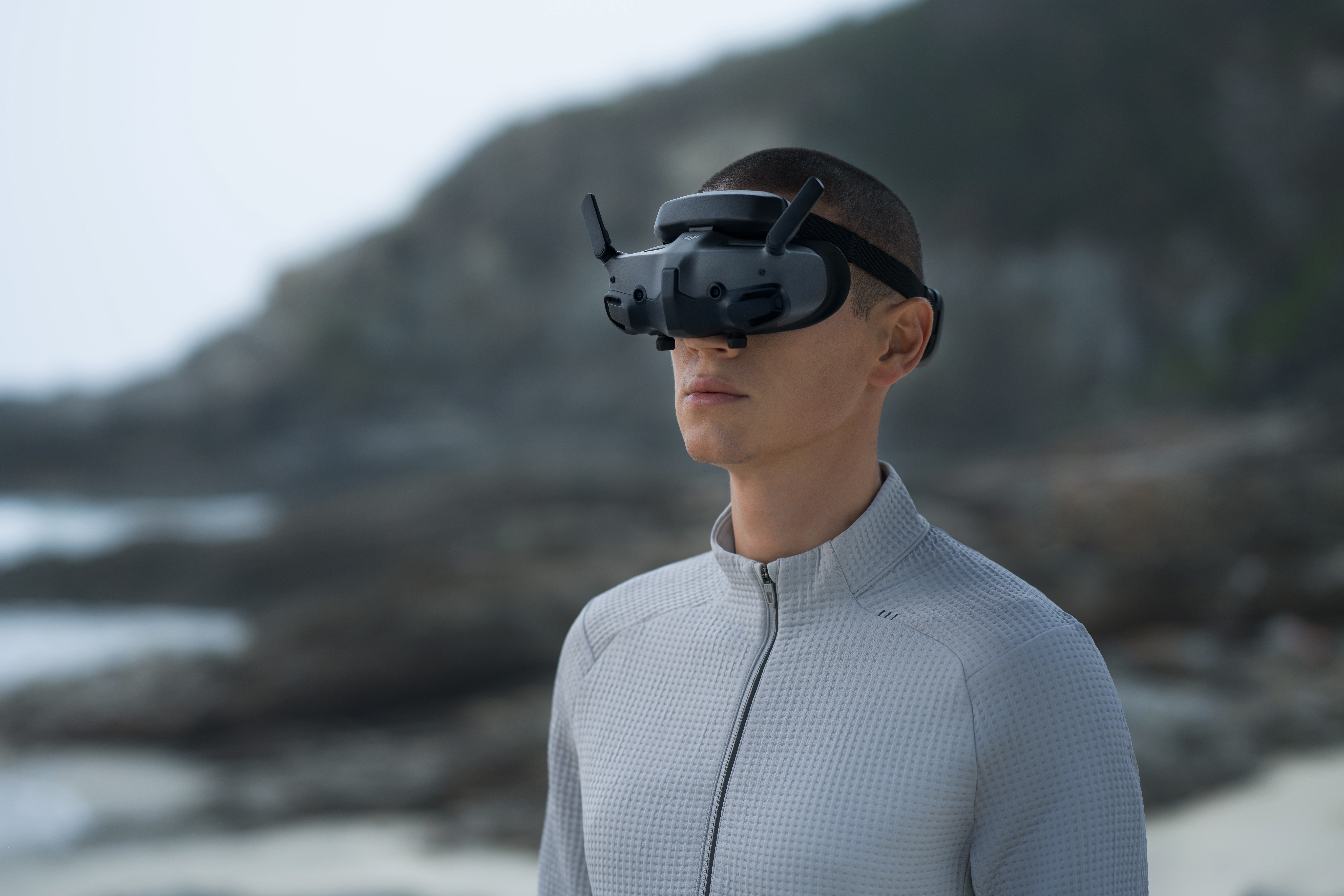 Un homme portant des lunettes VR se tient près de la côte. L'arrière-plan montre des rochers et le ciel flous.