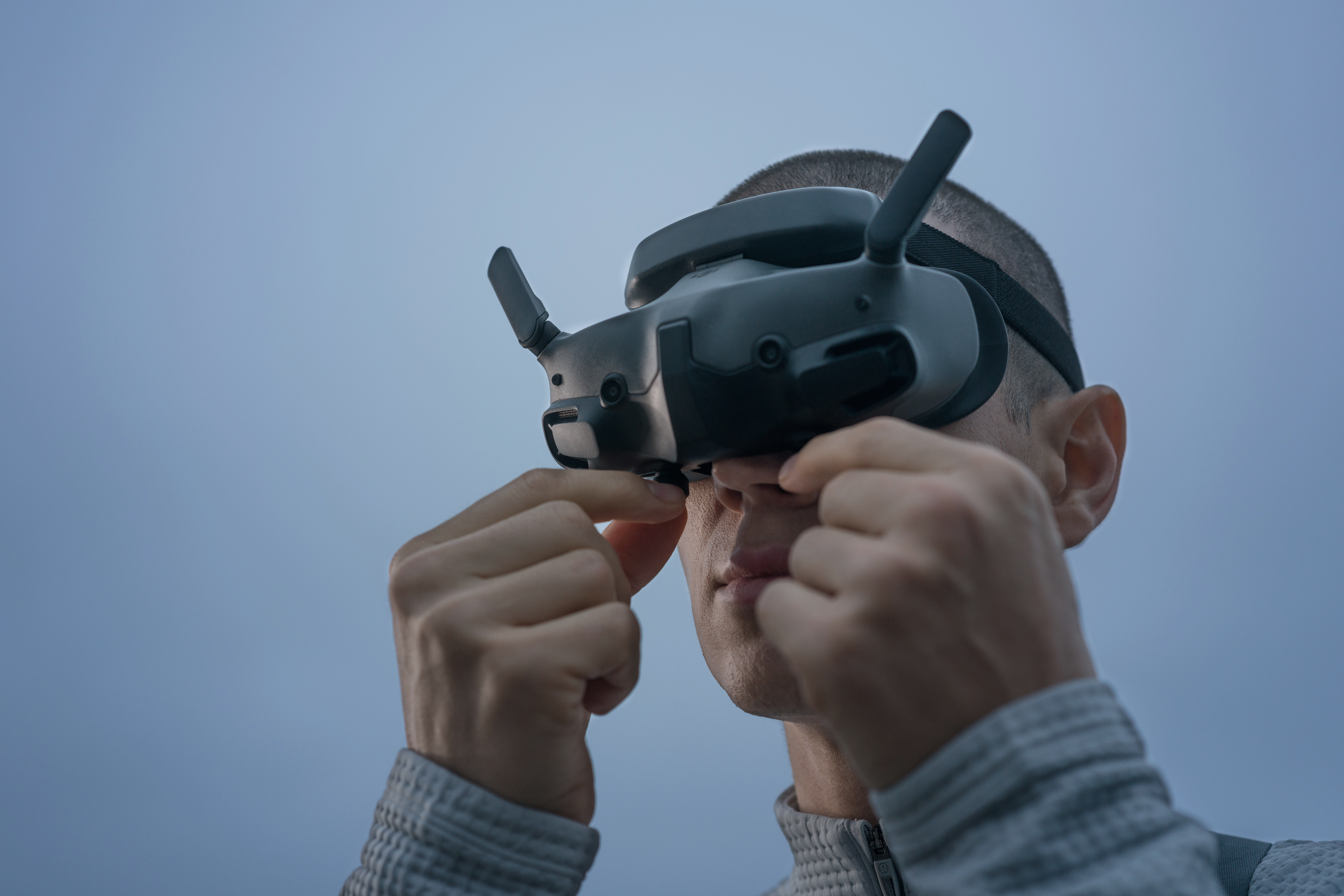 Un homme portant des lunettes VR les ajuste avec ses mains. Le fond est un ciel bleu clair.