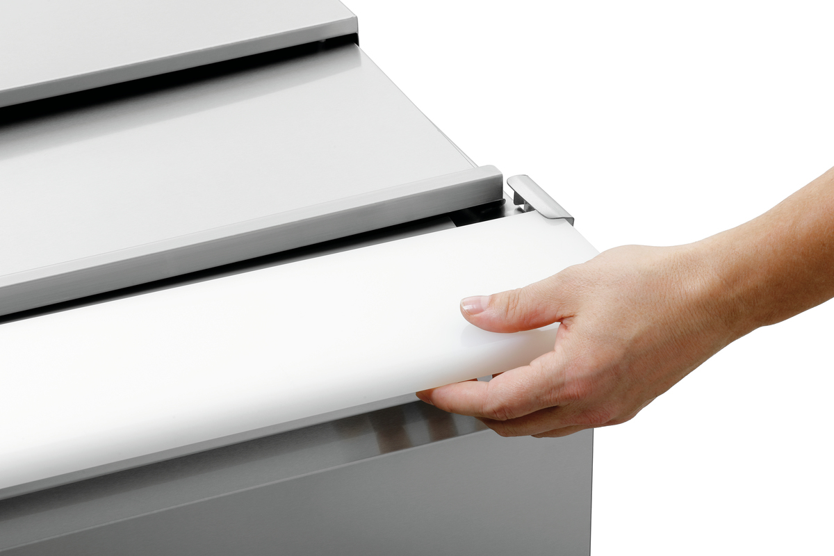 Eine Hand hält einen weißen, rechteckigen Gegenstand. Es liegt auf einer metallischen, rechteckigen Oberfläche. Der Hintergrund ist weiß.