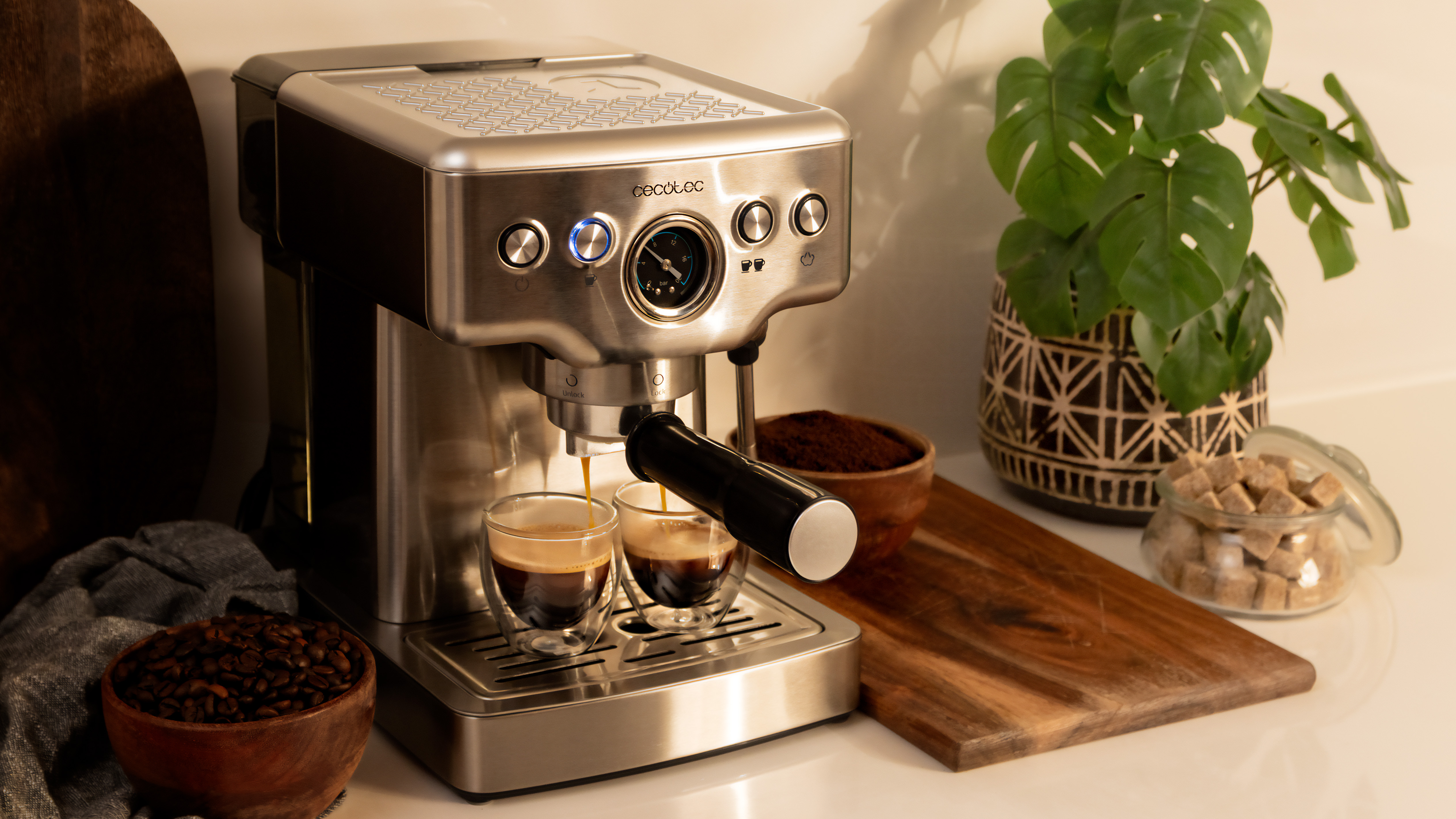 Una cafetera con dos vasos de café que se vierten. Hay granos de café y terrones de azúcar.
