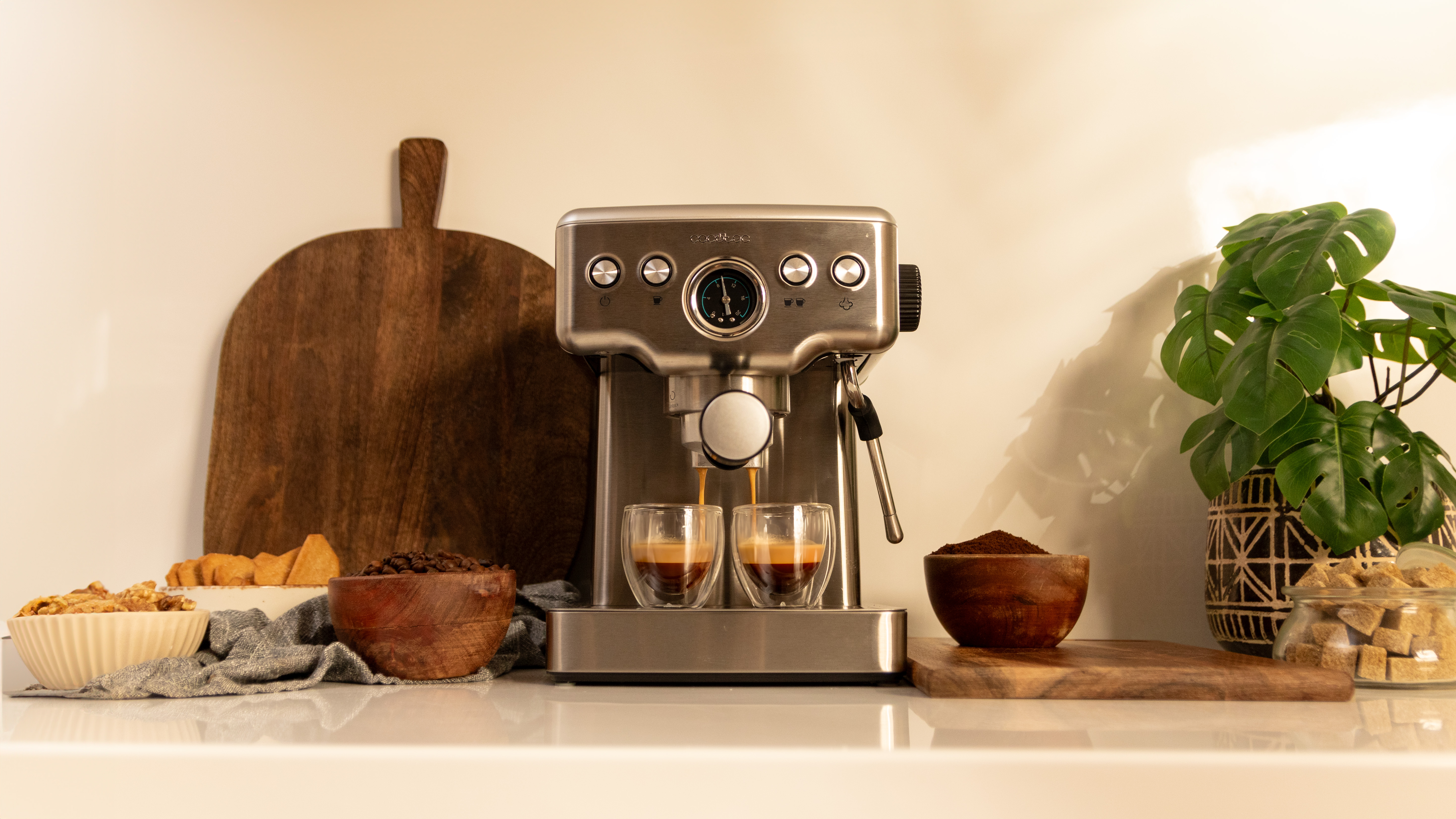 Máquina de espresso vertiendo café en dos tazas de vidrio. Tablas y cuencos de madera con granos y azúcar.