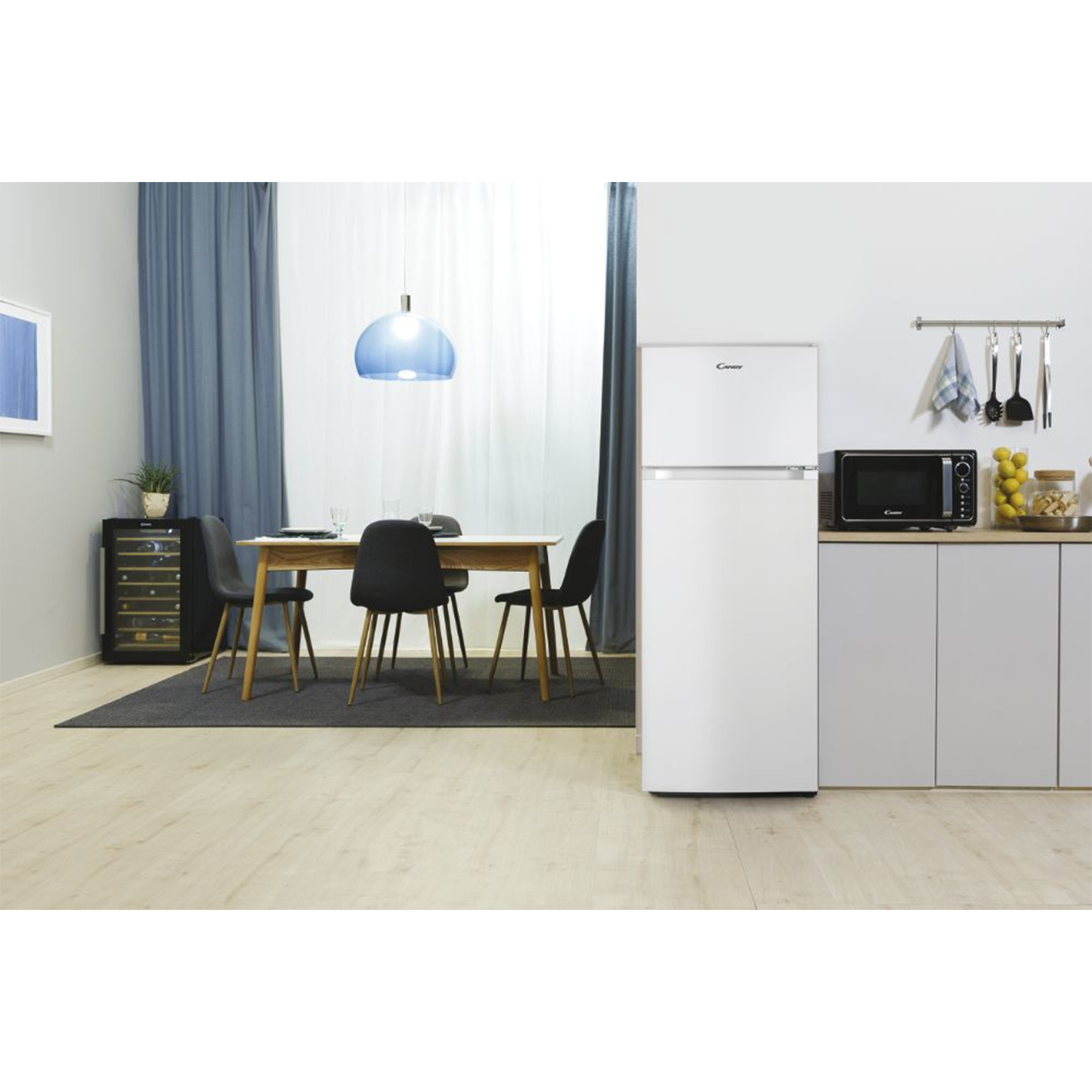 Cucina con frigorifero bianco, microonde e tavolo da pranzo. Tende blu sullo sfondo.
