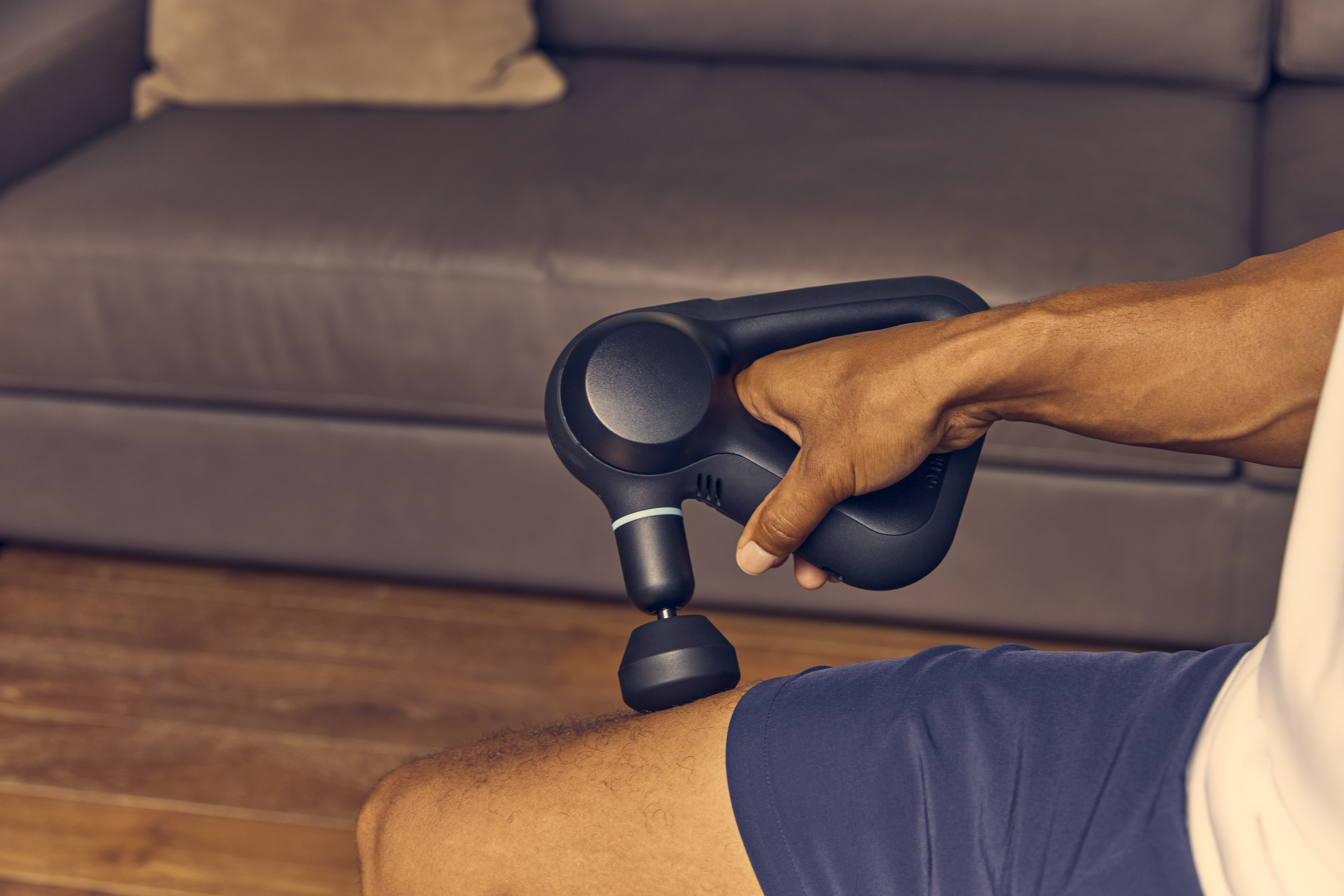 Eine Person massiert ein Bein mit einer schwarzen Massagepistole.