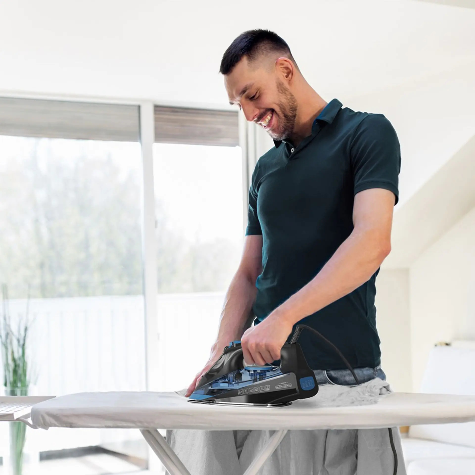 Mężczyzna prasujący koszulę na desce do prasowania czarnym żelazkiem.